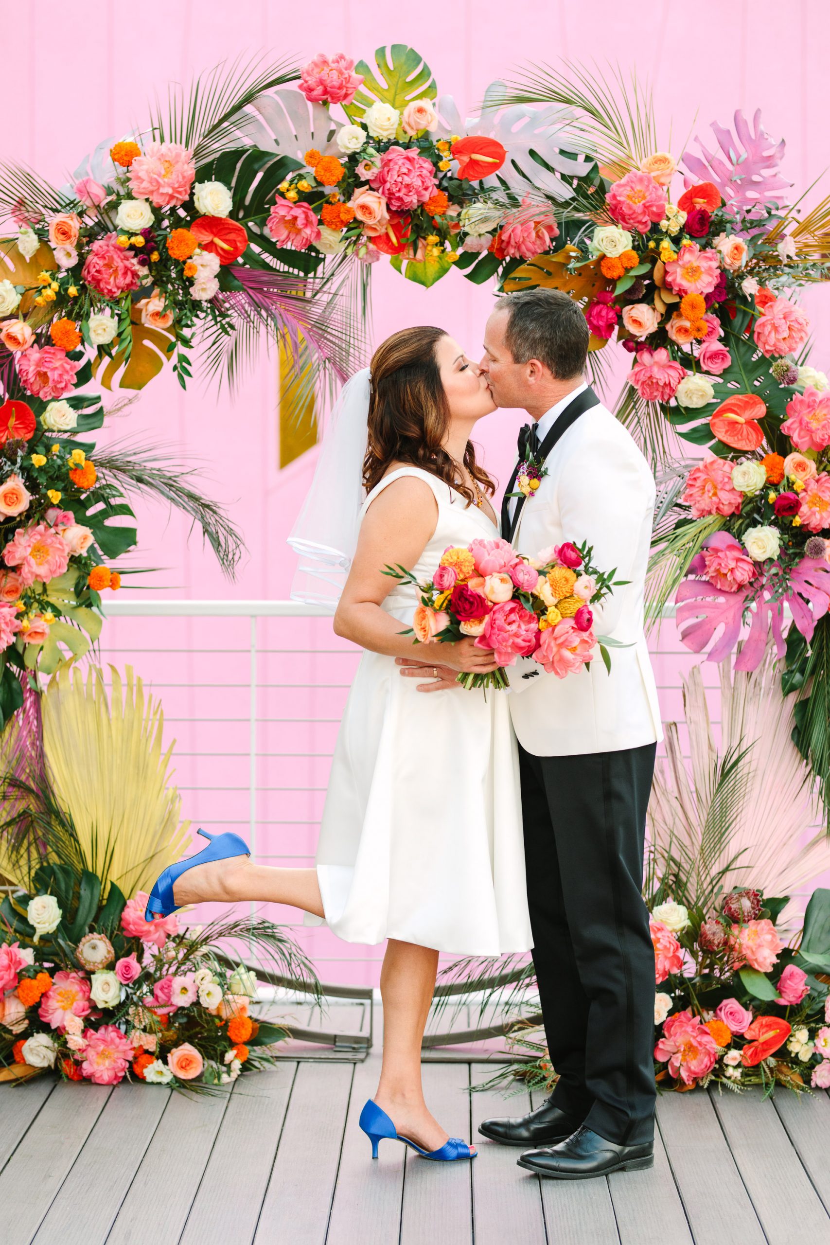 Couple kissing at colorful wedding ceremony arch www.marycostaweddings.com