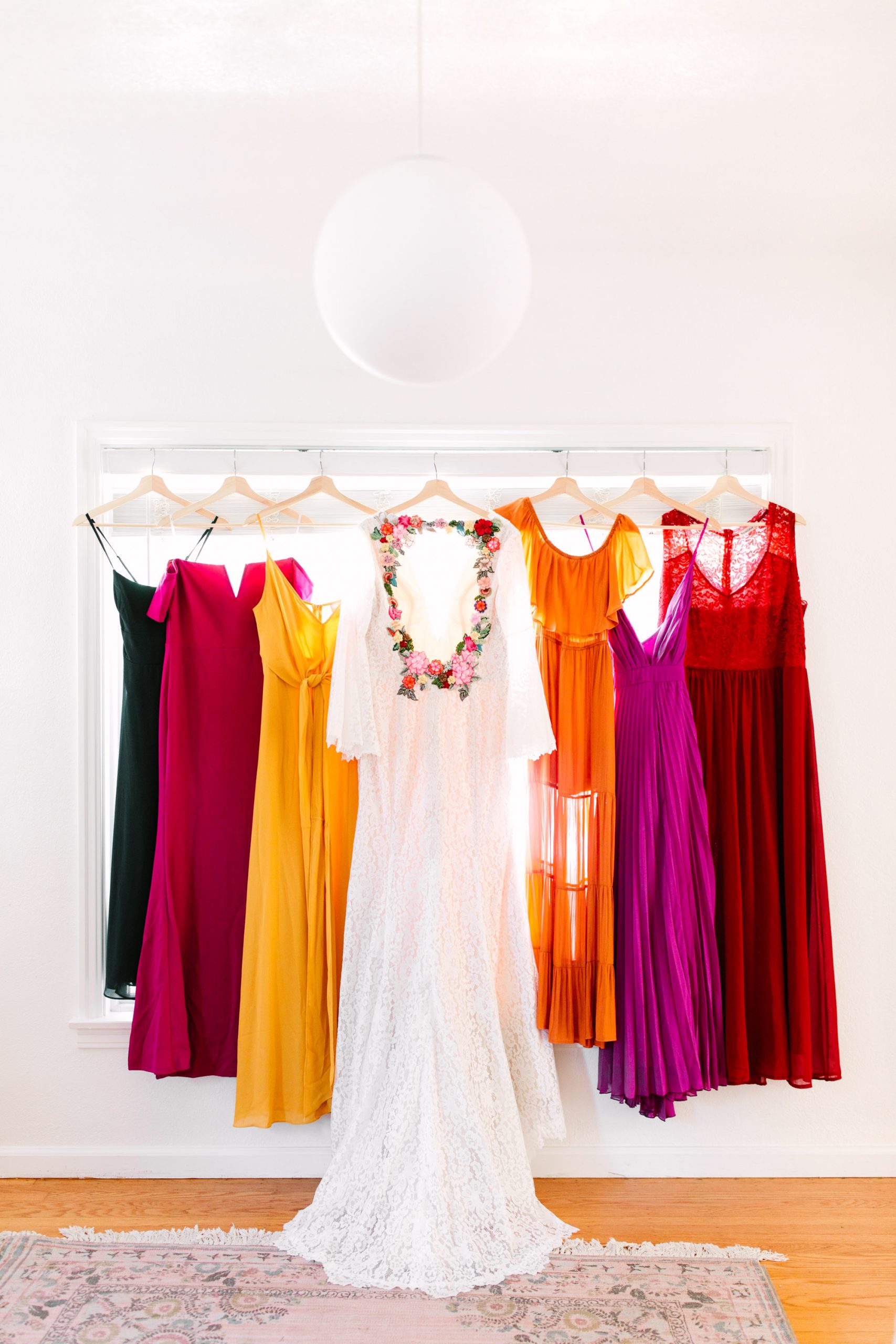 Custom embroidered bridal gown hanging with colorful assorted bridesmaids dresses - www.marycostaweddings.com