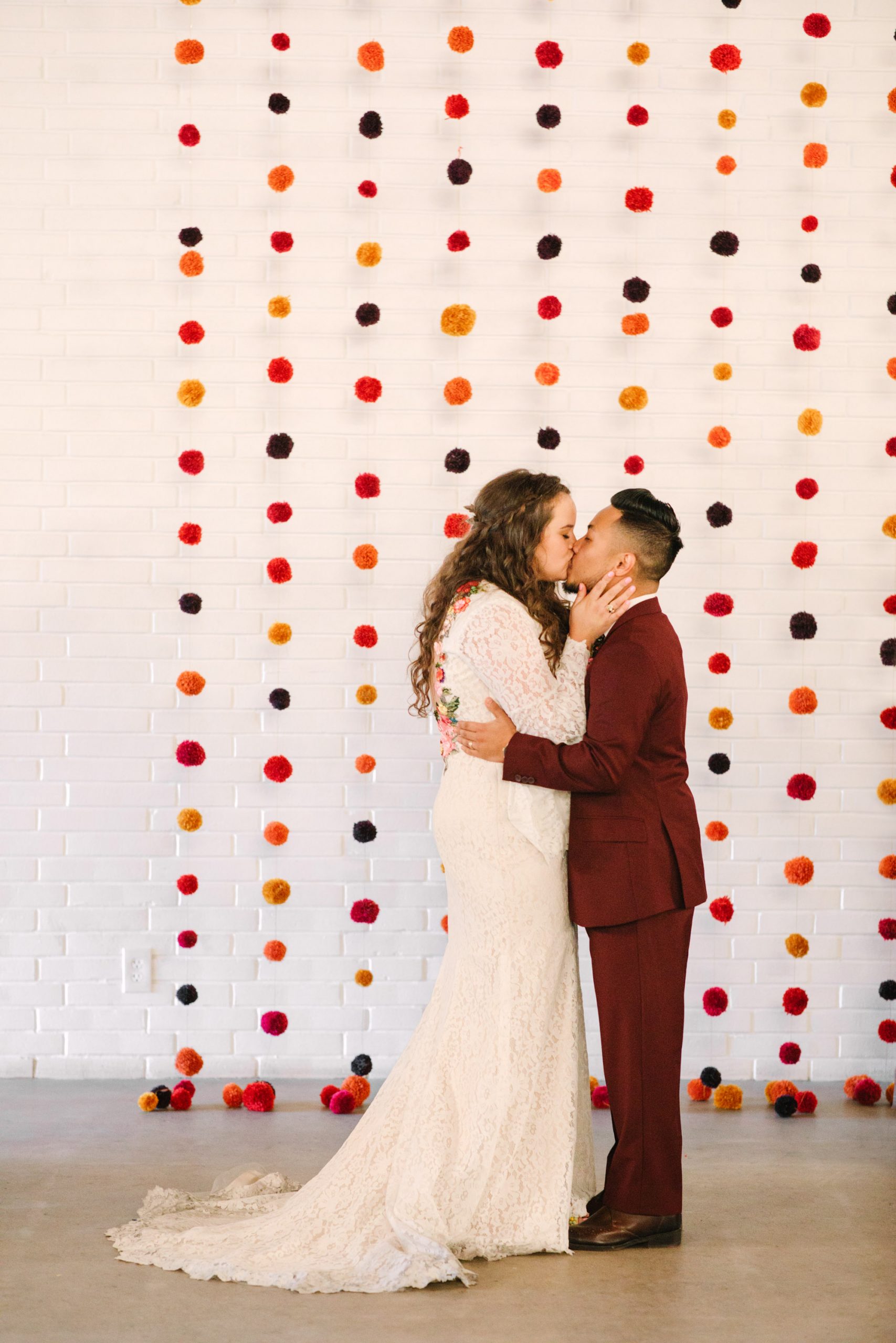 Bride and groom first kiss at wedding ceremony with pom pom backdrop at BLOC Venue Roseville - www.marycostaweddings.com