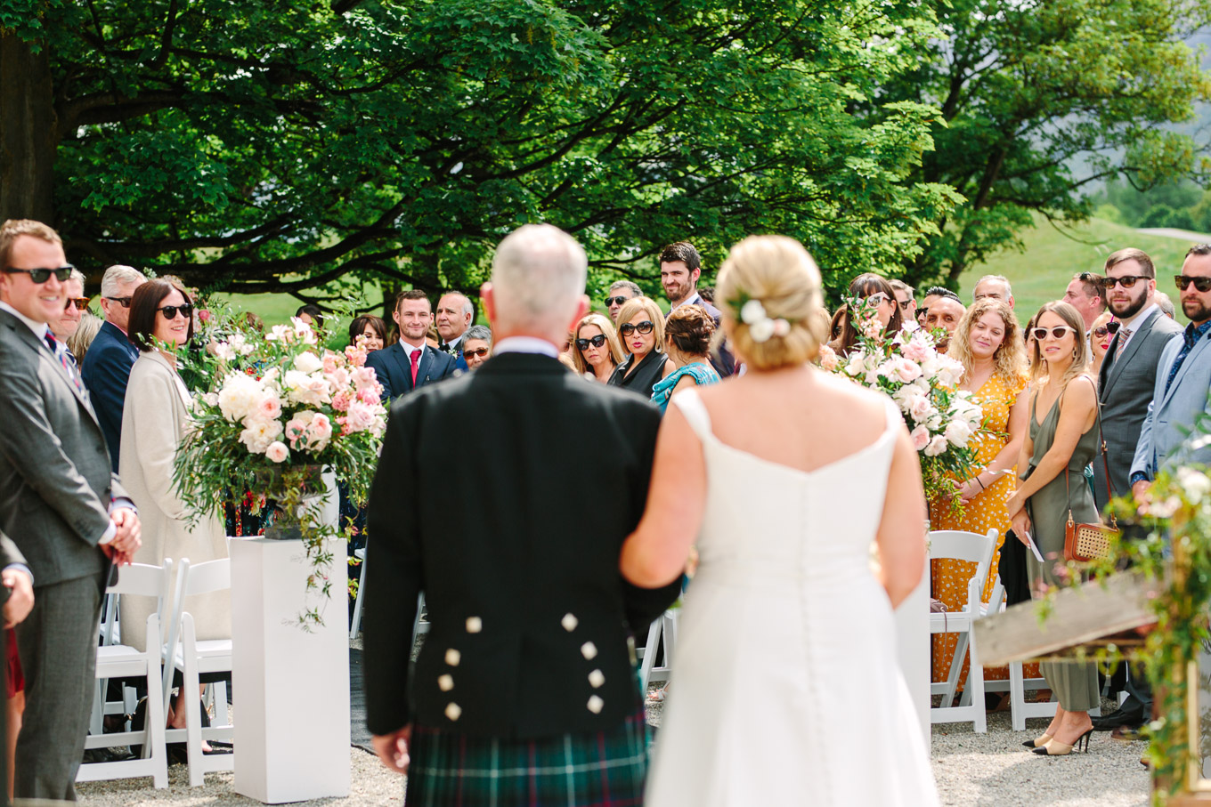 Bride and father in traditional Scottish kilt walking down the aisle at wedding ceremony. 