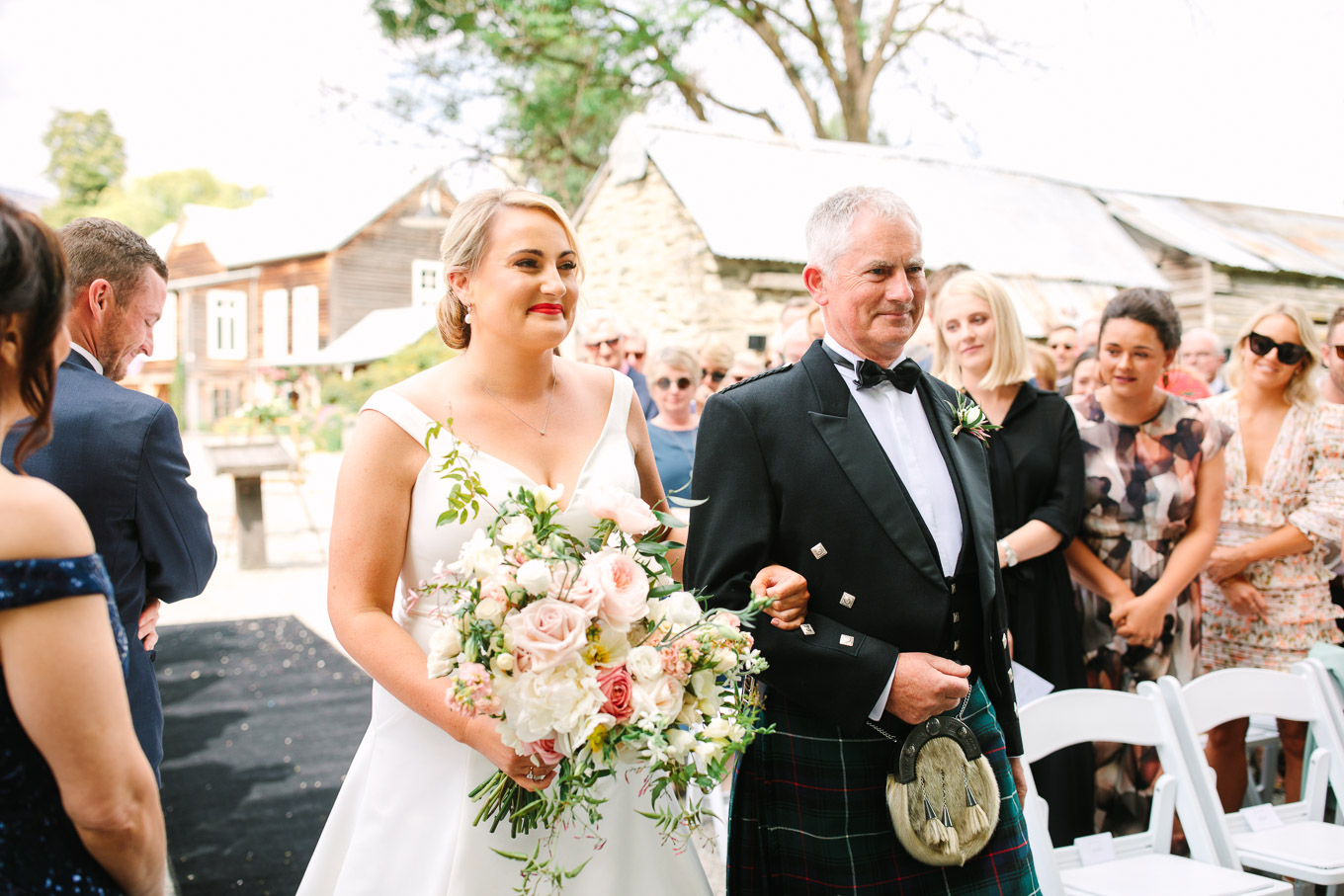 Bride and father in traditional Scottish kilt walking down the aisle together. Millbrook Resort Queenstown New Zealand wedding by Mary Costa Photography | www.marycostaweddings.com