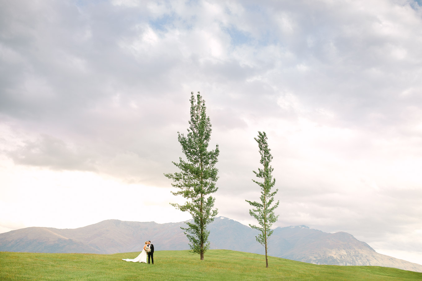 Wedding portrait with two trees on a hillside with Southern Alps in the background. Millbrook Resort Queenstown New Zealand wedding by Mary Costa Photography | www.marycostaweddings.com