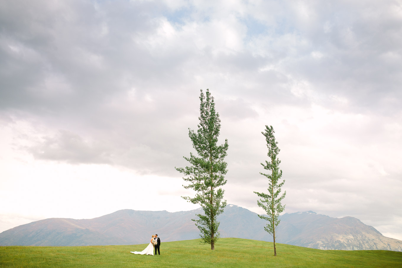 Wedding portrait with two trees on a hillside with Southern Alps in the background. Millbrook Resort Queenstown New Zealand wedding by Mary Costa Photography | www.marycostaweddings.com