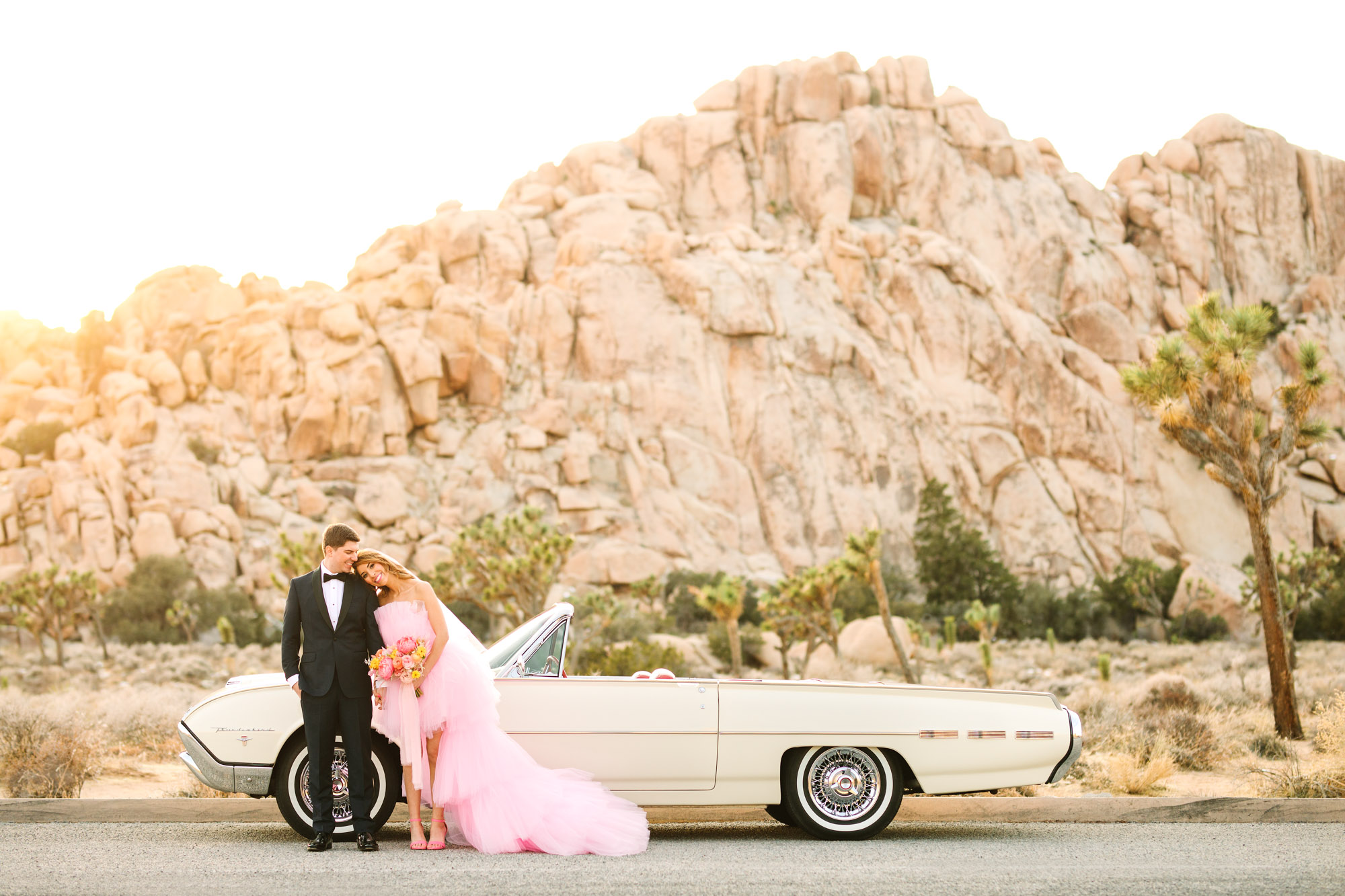 Bride and groom with a white classic Ford Thunderbird convertible car | Pink wedding dress Joshua Tree elopement featured on Green Wedding Shoes | Colorful desert wedding inspiration for fun-loving couples in Southern California #joshuatreewedding #joshuatreeelopement #pinkwedding #greenweddingshoes Source: Mary Costa Photography | Los Angeles
