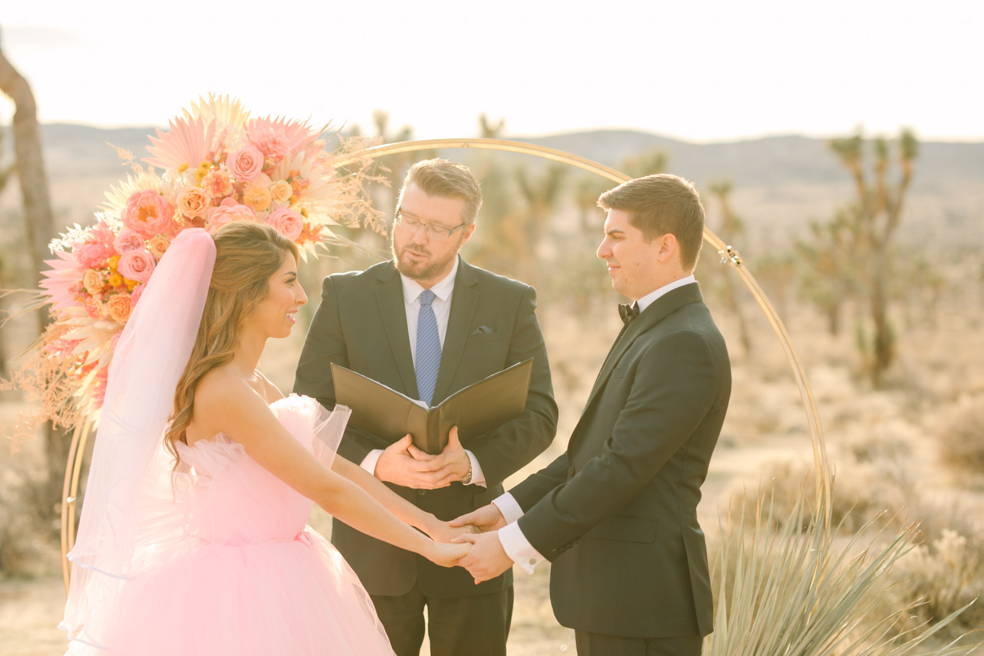 Bride and groom during elopement ceremony | Pink wedding dress Joshua Tree elopement featured on Green Wedding Shoes | Colorful desert wedding inspiration for fun-loving couples in Southern California #joshuatreewedding #joshuatreeelopement #pinkwedding #greenweddingshoes Source: Mary Costa Photography | Los Angeles