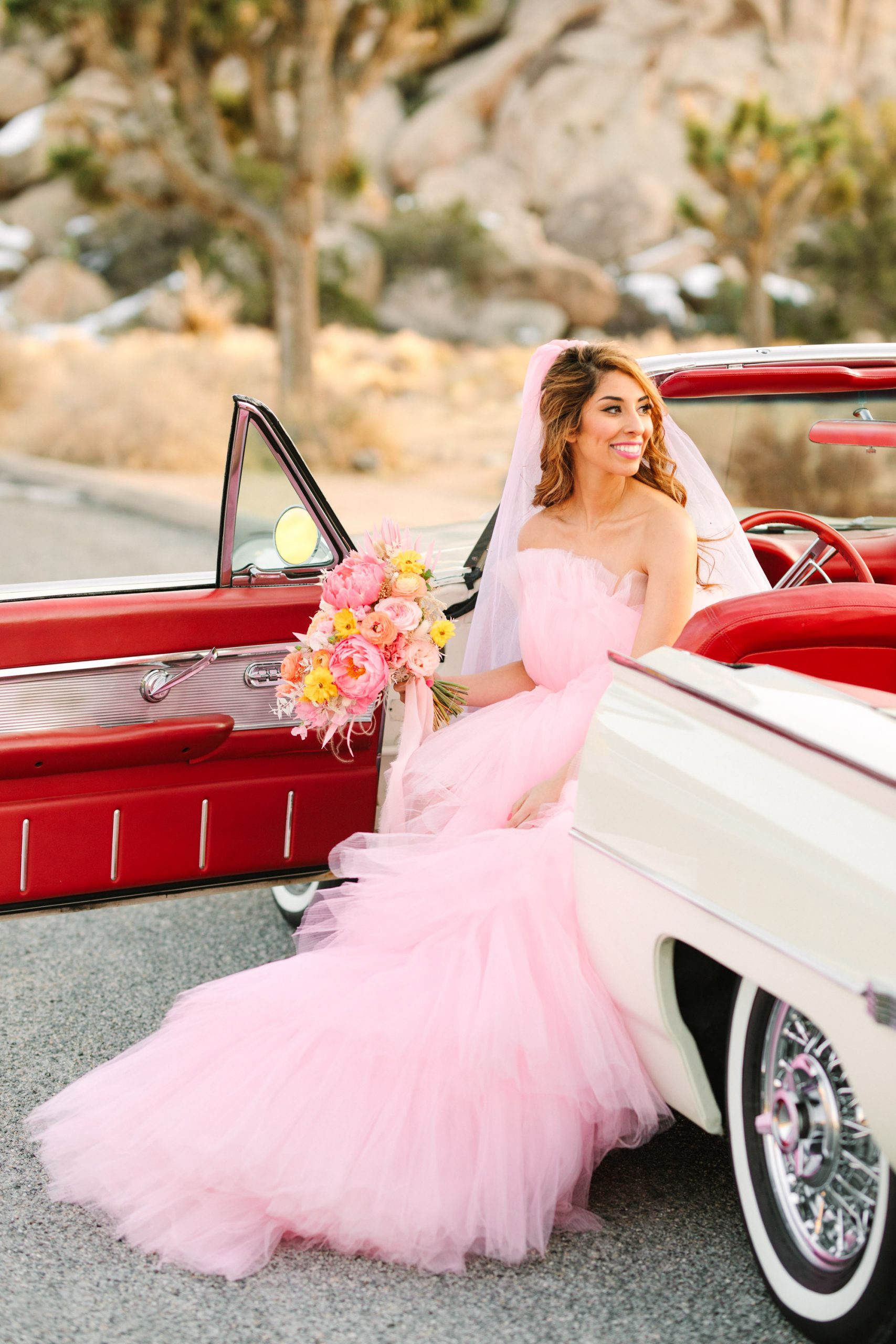 Bride sitting in white classic Ford Thunderbird convertible | Pink wedding dress Joshua Tree elopement featured on Green Wedding Shoes | Colorful desert wedding inspiration for fun-loving couples in Southern California #joshuatreewedding #joshuatreeelopement #pinkwedding #greenweddingshoes Source: Mary Costa Photography | Los Angeles