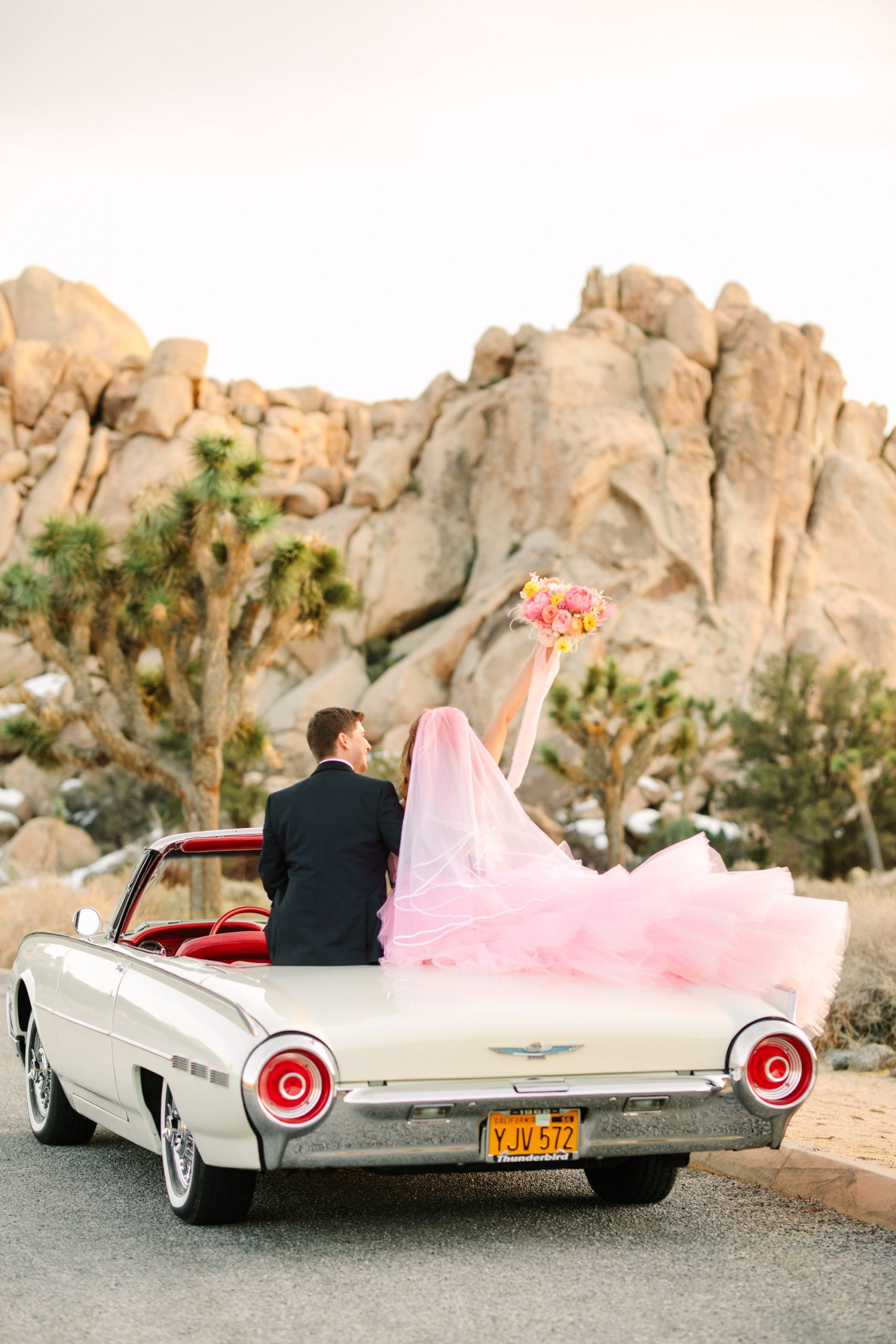 Bride and groom in white classic Ford Thunderbird convertible | Pink wedding dress Joshua Tree elopement featured on Green Wedding Shoes | Colorful desert wedding inspiration for fun-loving couples in Southern California #joshuatreewedding #joshuatreeelopement #pinkwedding #greenweddingshoes Source: Mary Costa Photography | Los Angeles