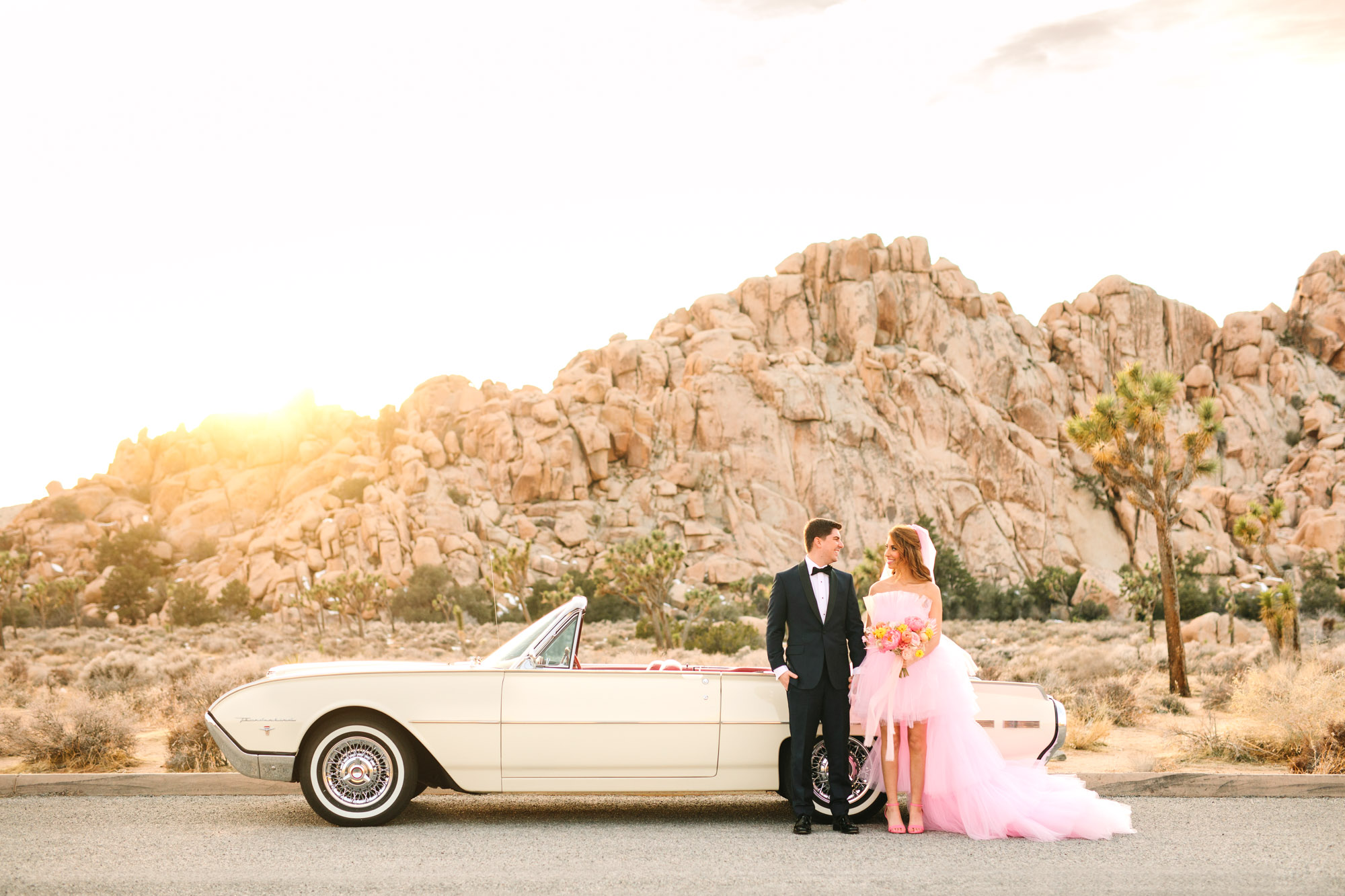 Bride and groom with white classic Ford Thunderbird | Pink wedding dress Joshua Tree elopement featured on Green Wedding Shoes | Colorful desert wedding inspiration for fun-loving couples in Southern California #joshuatreewedding #joshuatreeelopement #pinkwedding #greenweddingshoes Source: Mary Costa Photography | Los Angeles