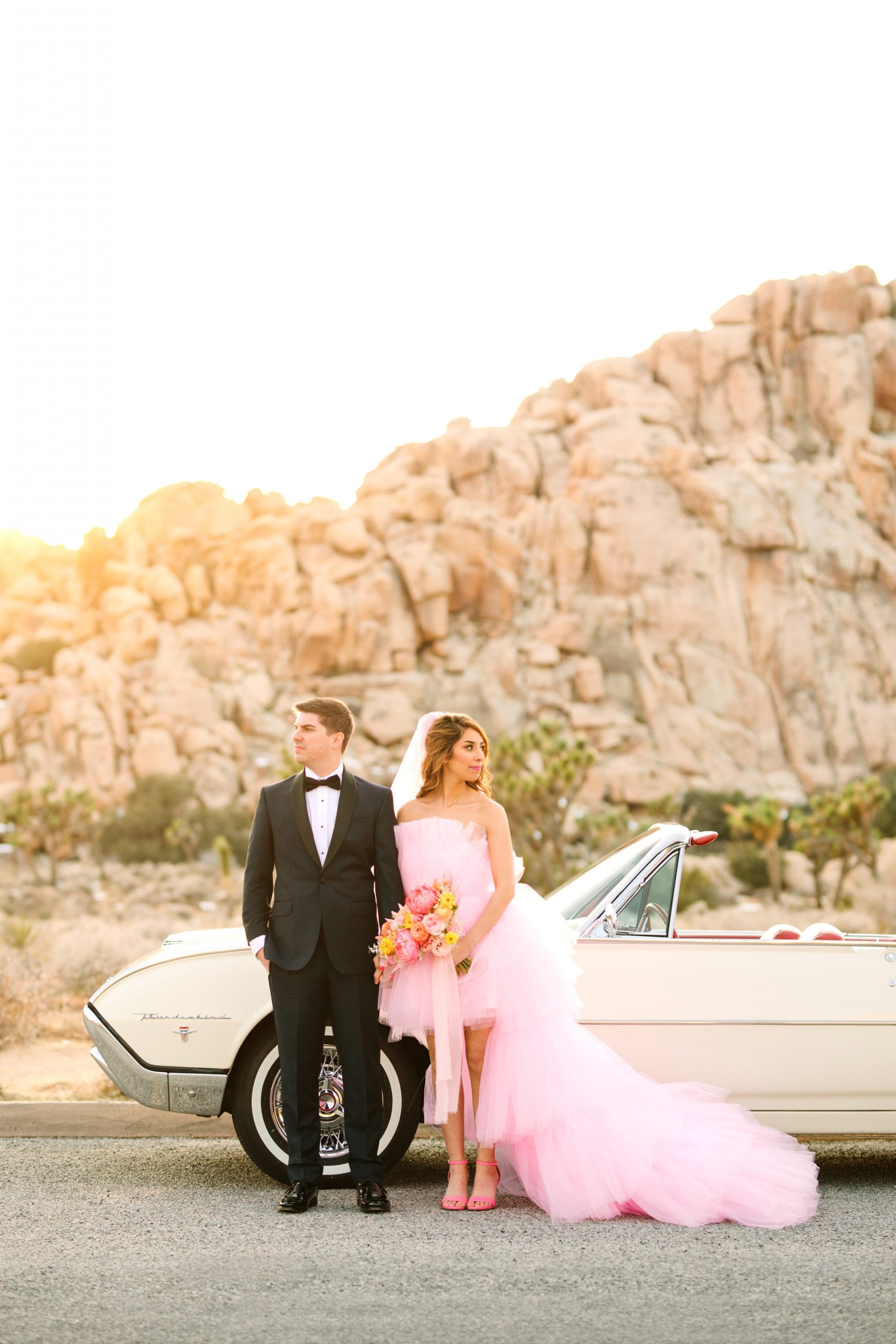 Bride and groom with white classic convertible car | Pink wedding dress Joshua Tree elopement featured on Green Wedding Shoes | Colorful desert wedding inspiration for fun-loving couples in Southern California #joshuatreewedding #joshuatreeelopement #pinkwedding #greenweddingshoes Source: Mary Costa Photography | Los Angeles
