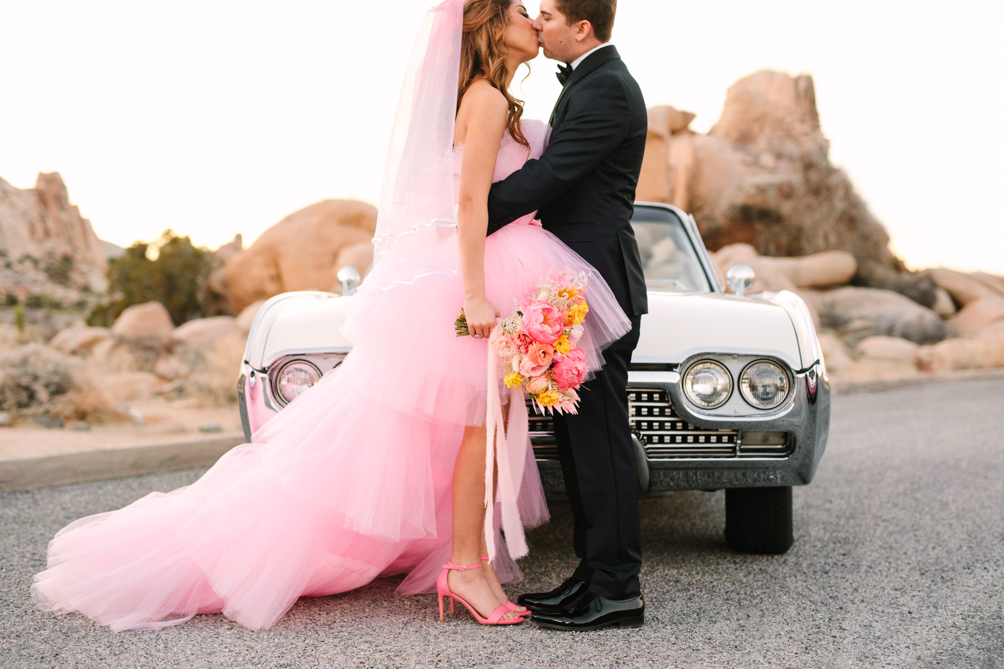 Bride and groom in front of white classic convertible car | Pink wedding dress Joshua Tree elopement featured on Green Wedding Shoes | Colorful desert wedding inspiration for fun-loving couples in Southern California #joshuatreewedding #joshuatreeelopement #pinkwedding #greenweddingshoes Source: Mary Costa Photography | Los Angeles