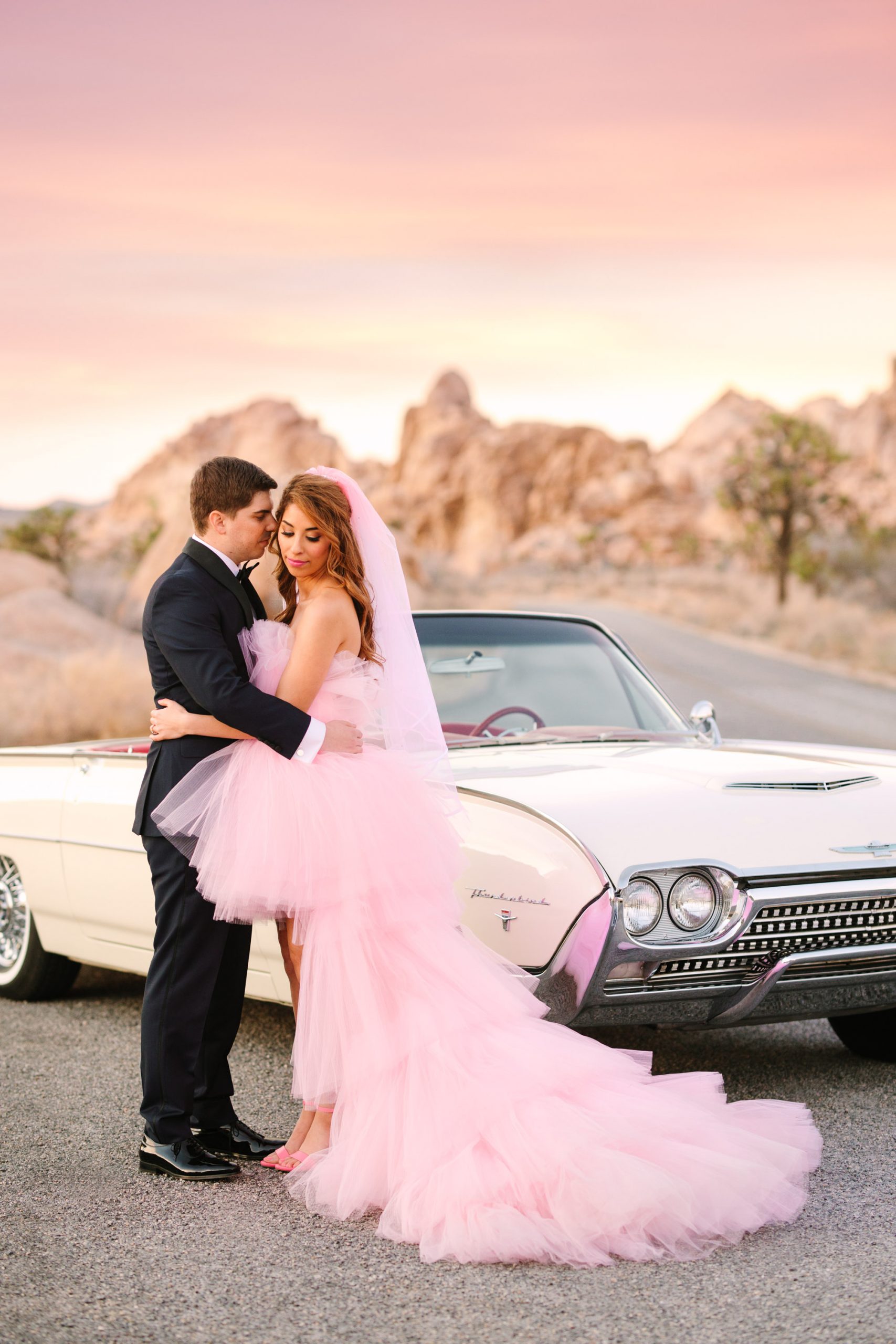Bride and groom with white classic convertible | Pink wedding dress Joshua Tree elopement featured on Green Wedding Shoes | Colorful desert wedding inspiration for fun-loving couples in Southern California #joshuatreewedding #joshuatreeelopement #pinkwedding #greenweddingshoes Source: Mary Costa Photography | Los Angeles
