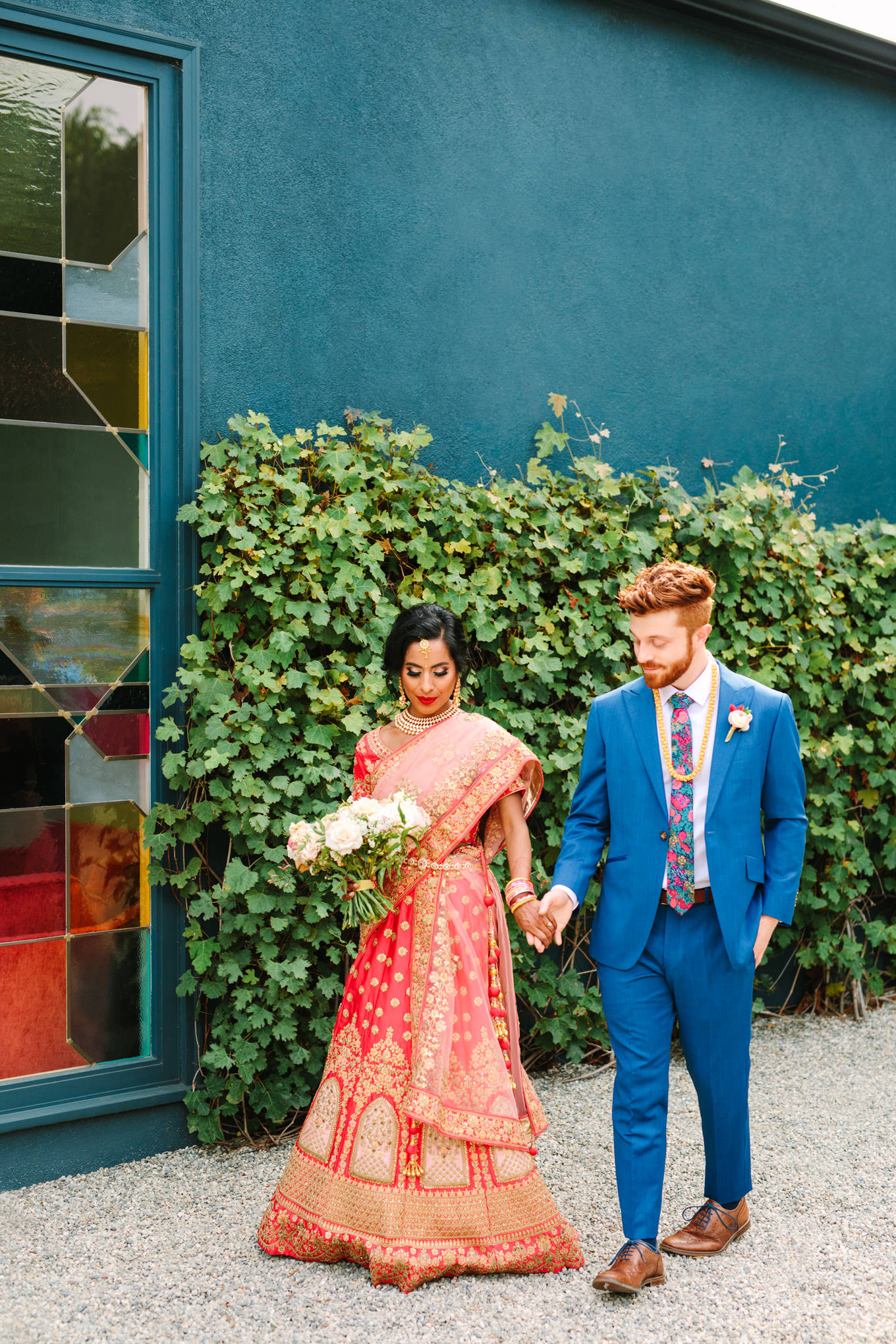 Bride in red saree and groom in blue suit walking together. Two Disney artists create a unique and colorful Indian Fusion wedding at The Fig House Los Angeles, featured on Green Wedding Shoes. | Colorful and elevated wedding inspiration for fun-loving couples in Southern California | #indianwedding #indianfusionwedding #thefighouse #losangeleswedding   Source: Mary Costa Photography | Los Angeles