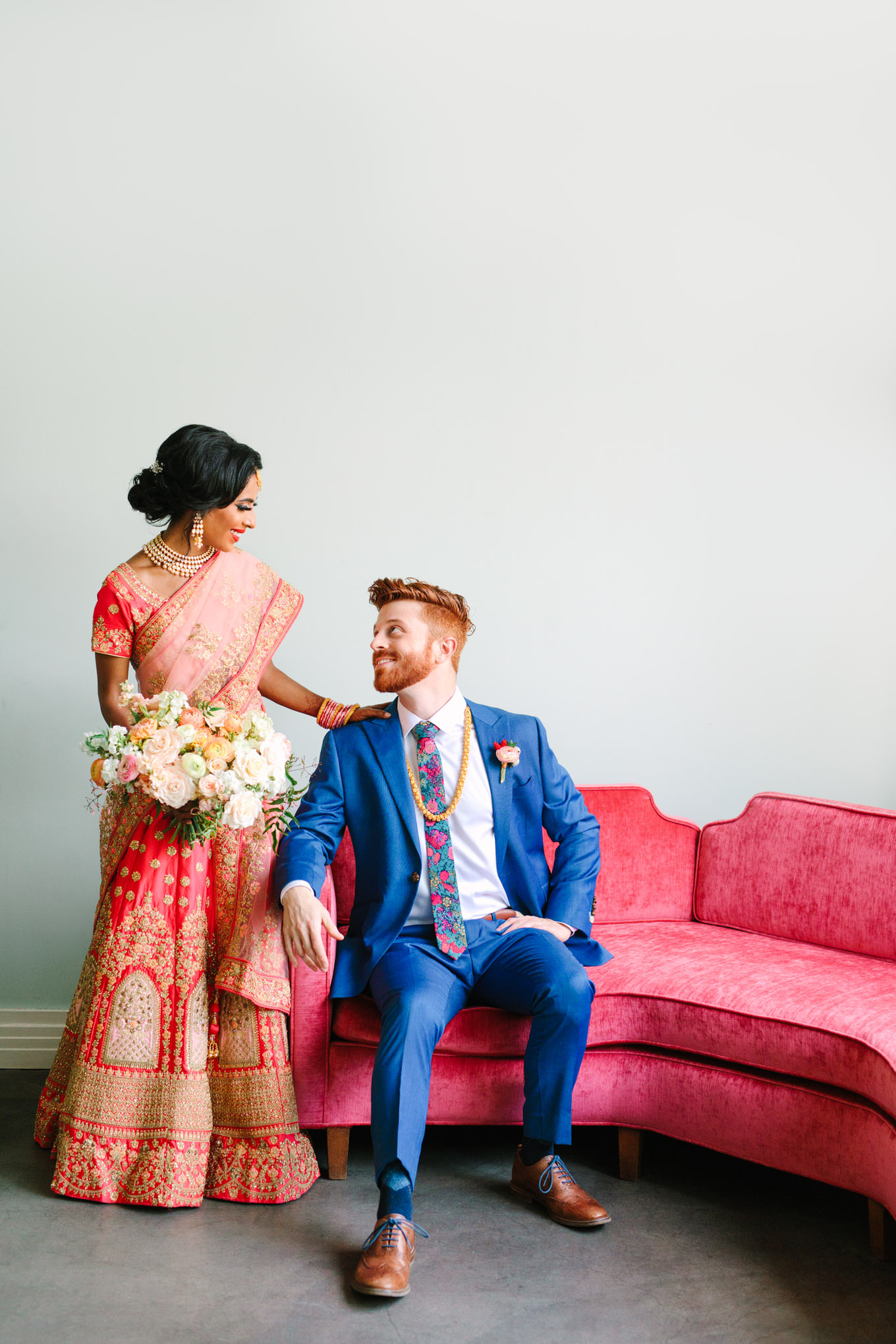 Bride and groom sitting on pink couch. Two Disney artists create a unique and colorful Indian Fusion wedding at The Fig House Los Angeles, featured on Green Wedding Shoes. | Colorful and elevated wedding inspiration for fun-loving couples in Southern California | #indianwedding #indianfusionwedding #thefighouse #losangeleswedding   Source: Mary Costa Photography | Los Angeles