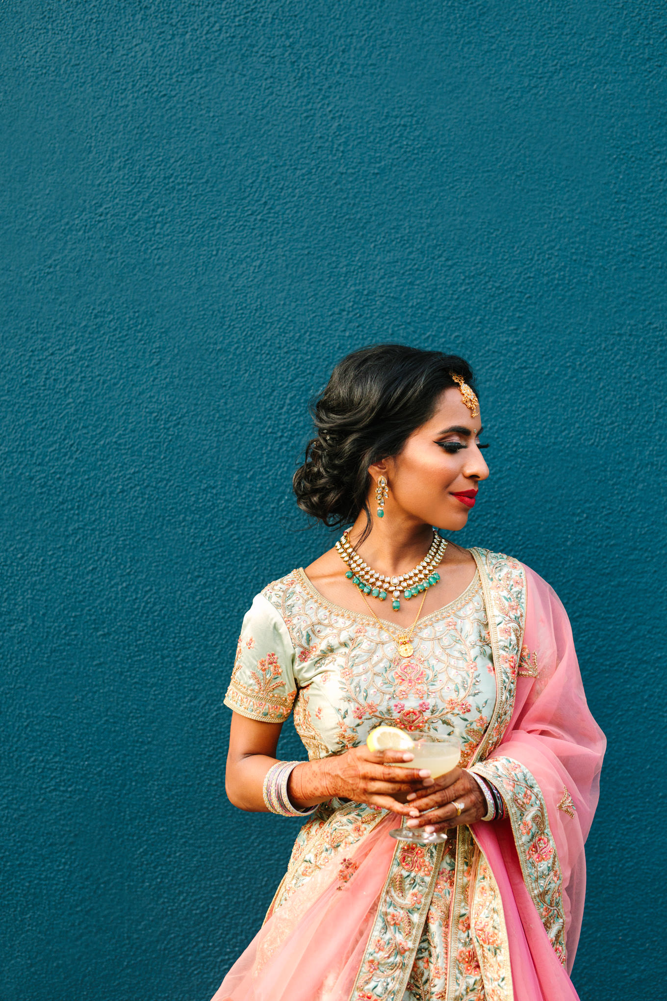 Bride with cocktail in front of teal wall. Two Disney artists create a unique and colorful Indian Fusion wedding at The Fig House Los Angeles, featured on Green Wedding Shoes. | Colorful and elevated wedding inspiration for fun-loving couples in Southern California | #indianwedding #indianfusionwedding #thefighouse #losangeleswedding   Source: Mary Costa Photography | Los Angeles