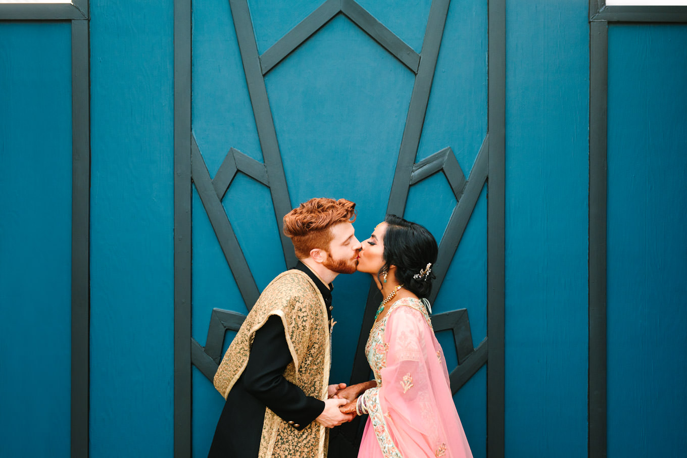 Bride and groom kissing in front of geometric bold door. Two Disney artists create a unique and colorful Indian Fusion wedding at The Fig House Los Angeles, featured on Green Wedding Shoes. | Colorful and elevated wedding inspiration for fun-loving couples in Southern California | #indianwedding #indianfusionwedding #thefighouse #losangeleswedding   Source: Mary Costa Photography | Los Angeles