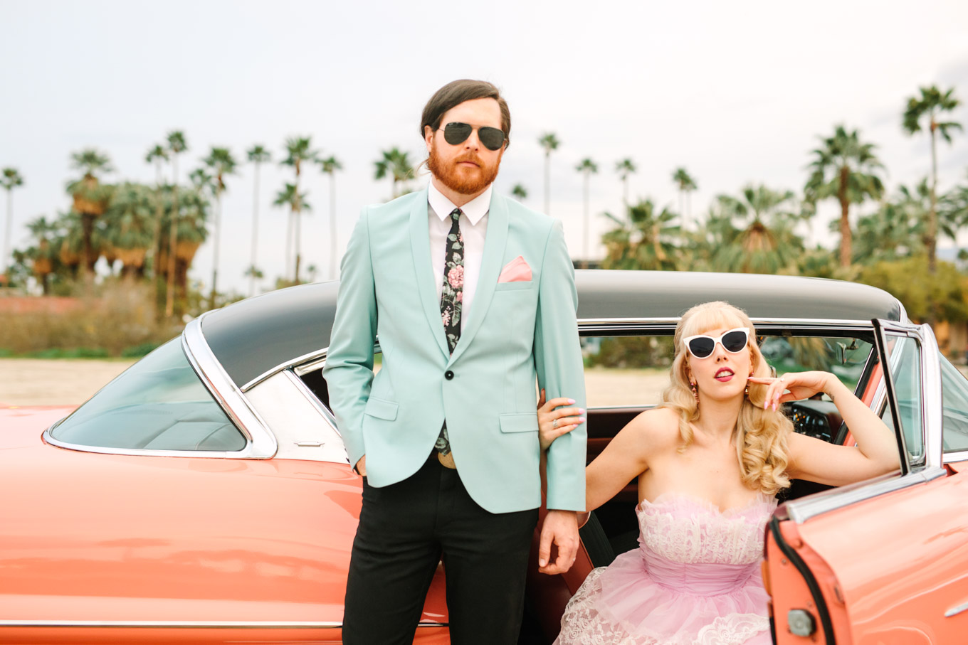 Retro-inspired couple in sunglasses. Modern vintage-inspired Palm Springs engagement session with a 1960s pink Cadillac, retro clothing, and flowers by Shindig Chic. | Colorful and elevated wedding inspiration for fun-loving couples in Southern California | #engagementsession #PalmSpringsengagement #vintageweddingdress #floralcar #pinkcar   Source: Mary Costa Photography | Los Angeles