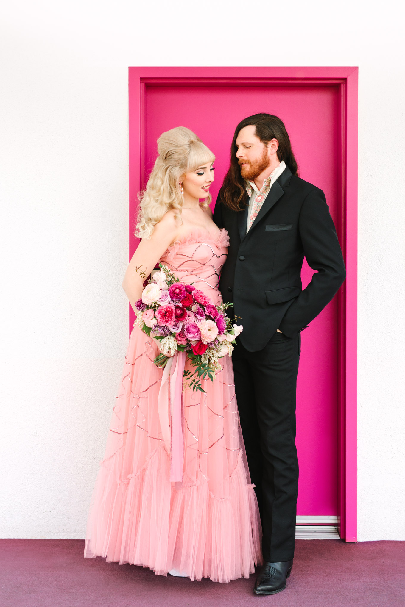 Retro couple with colorful Saguaro Hotel door. Modern vintage-inspired Palm Springs engagement session with a 1960s pink Cadillac, retro clothing, and flowers by Shindig Chic. | Colorful and elevated wedding inspiration for fun-loving couples in Southern California | #engagementsession #PalmSpringsengagement #vintageweddingdress #floralcar #pinkcar   Source: Mary Costa Photography | Los Angeles 
