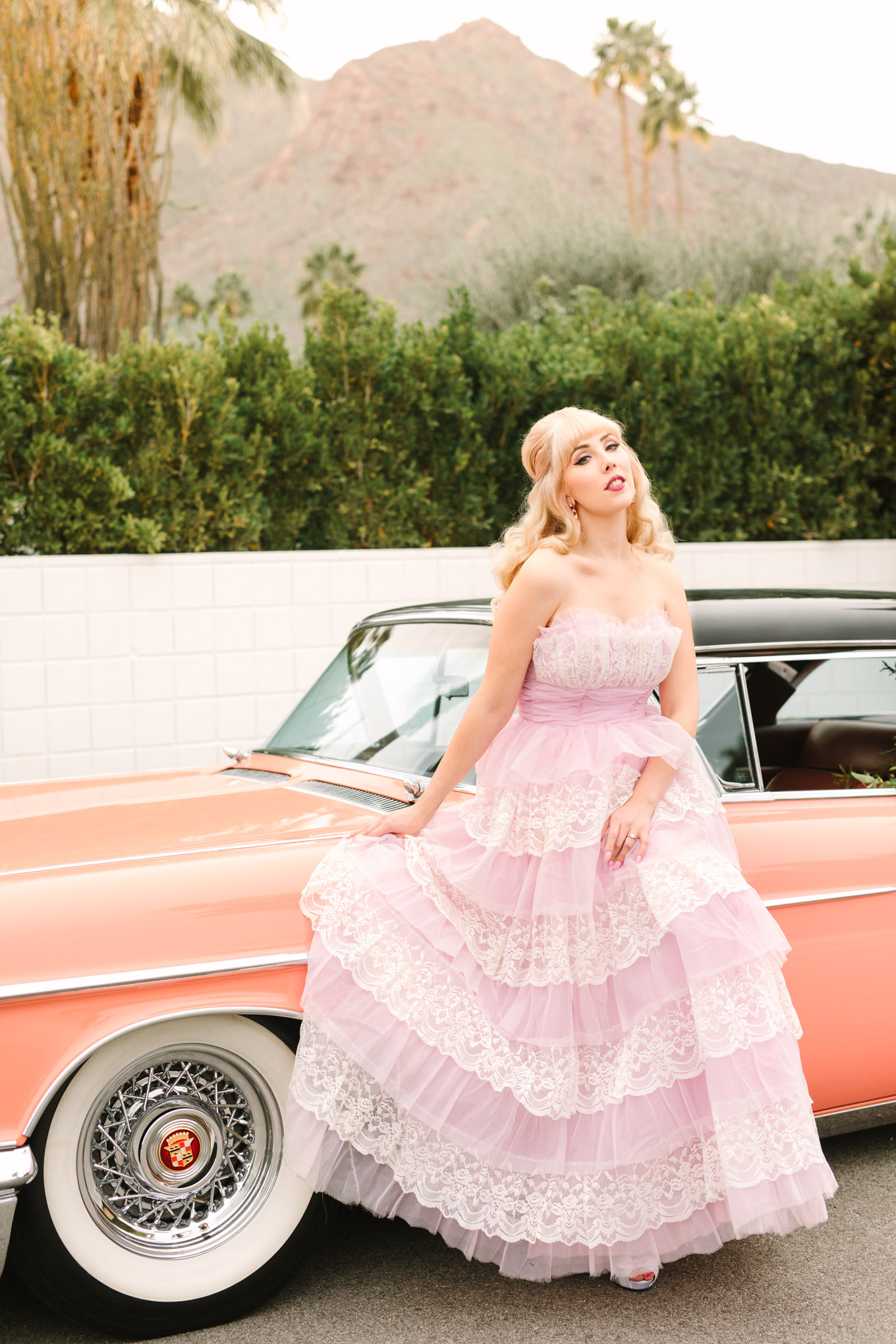 Bride in retro prom dress. Modern vintage-inspired Palm Springs engagement session with a 1960s pink Cadillac, retro clothing, and flowers by Shindig Chic. | Colorful and elevated wedding inspiration for fun-loving couples in Southern California | #engagementsession #PalmSpringsengagement #vintageweddingdress #floralcar #pinkcar   Source: Mary Costa Photography | Los Angeles