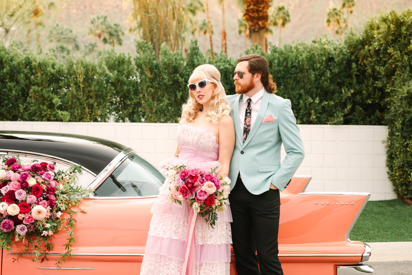 Colorful couple in retro clothing. Modern vintage-inspired Palm Springs engagement session with a 1960s pink Cadillac, retro clothing, and flowers by Shindig Chic. | Colorful and elevated wedding inspiration for fun-loving couples in Southern California | #engagementsession #PalmSpringsengagement #vintageweddingdress #floralcar #pinkcar   Source: Mary Costa Photography | Los Angeles