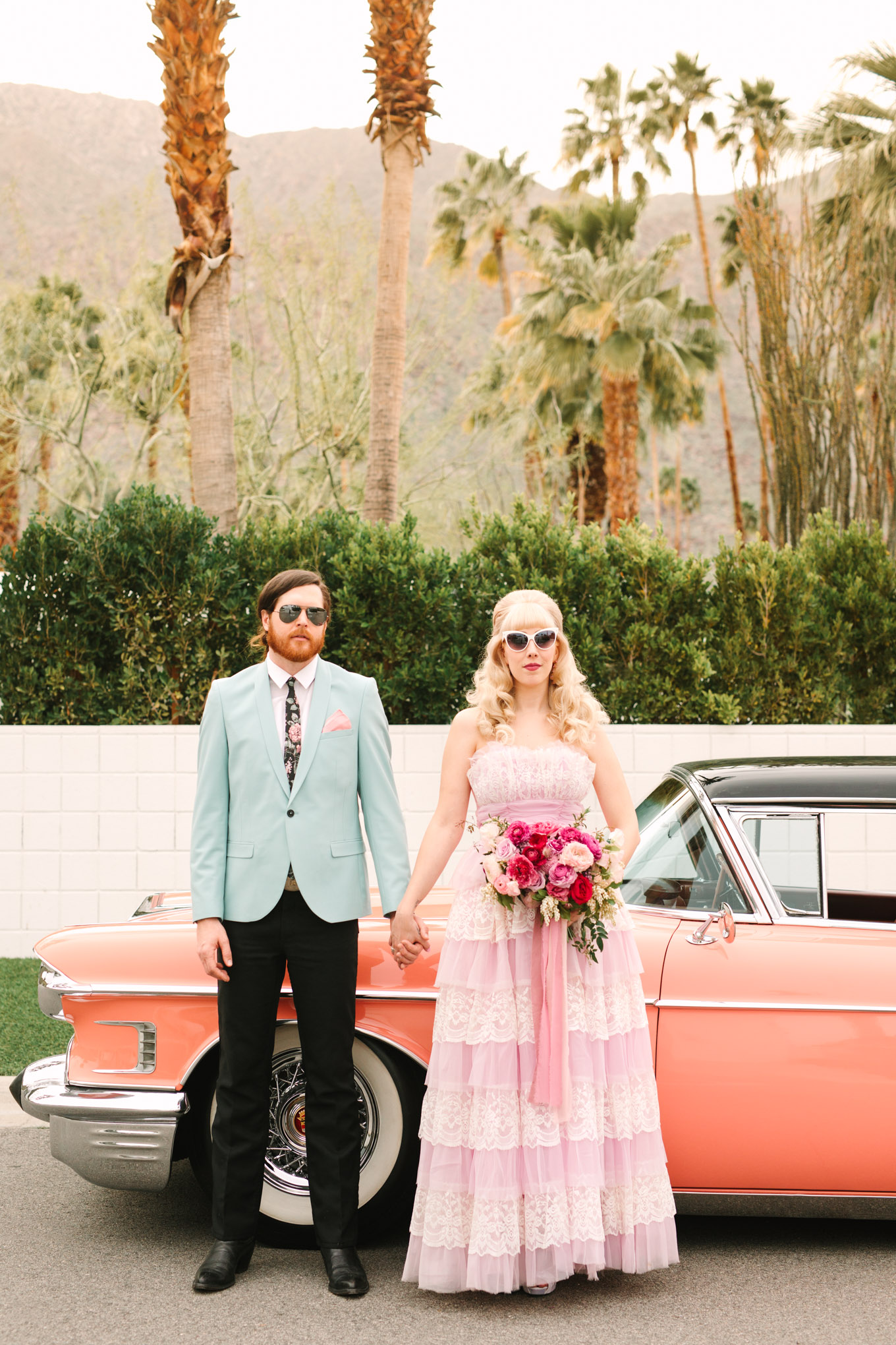 Retro couple with coral classic car. Modern vintage-inspired Palm Springs engagement session with a 1960s pink Cadillac, retro clothing, and flowers by Shindig Chic. | Colorful and elevated wedding inspiration for fun-loving couples in Southern California | #engagementsession #PalmSpringsengagement #vintageweddingdress #floralcar #pinkcar   Source: Mary Costa Photography | Los Angeles