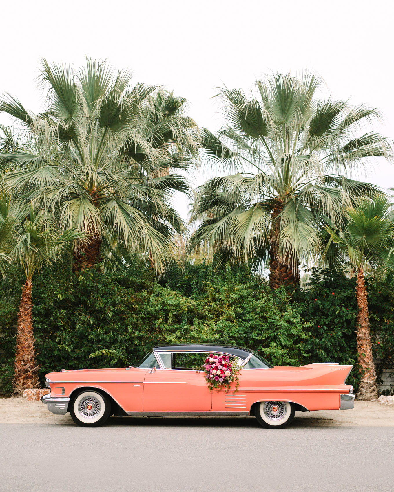 Coral classic car outside Casa De Monte Vista. Modern vintage-inspired Palm Springs engagement session with a 1960s pink Cadillac, retro clothing, and flowers by Shindig Chic. | Colorful and elevated wedding inspiration for fun-loving couples in Southern California | #engagementsession #PalmSpringsengagement #vintageweddingdress #floralcar #pinkcar   Source: Mary Costa Photography | Los Angeles