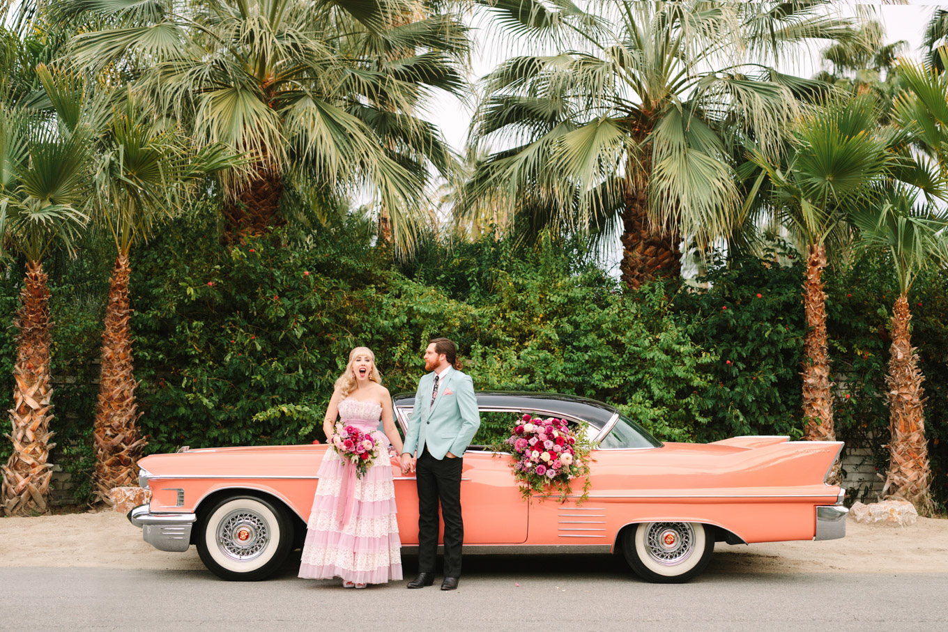 Retro couple outside of Casa De Monte Vista. Modern vintage-inspired Palm Springs engagement session with a 1960s pink Cadillac, retro clothing, and flowers by Shindig Chic. | Colorful and elevated wedding inspiration for fun-loving couples in Southern California | #engagementsession #PalmSpringsengagement #vintageweddingdress #floralcar #pinkcar   Source: Mary Costa Photography | Los Angeles