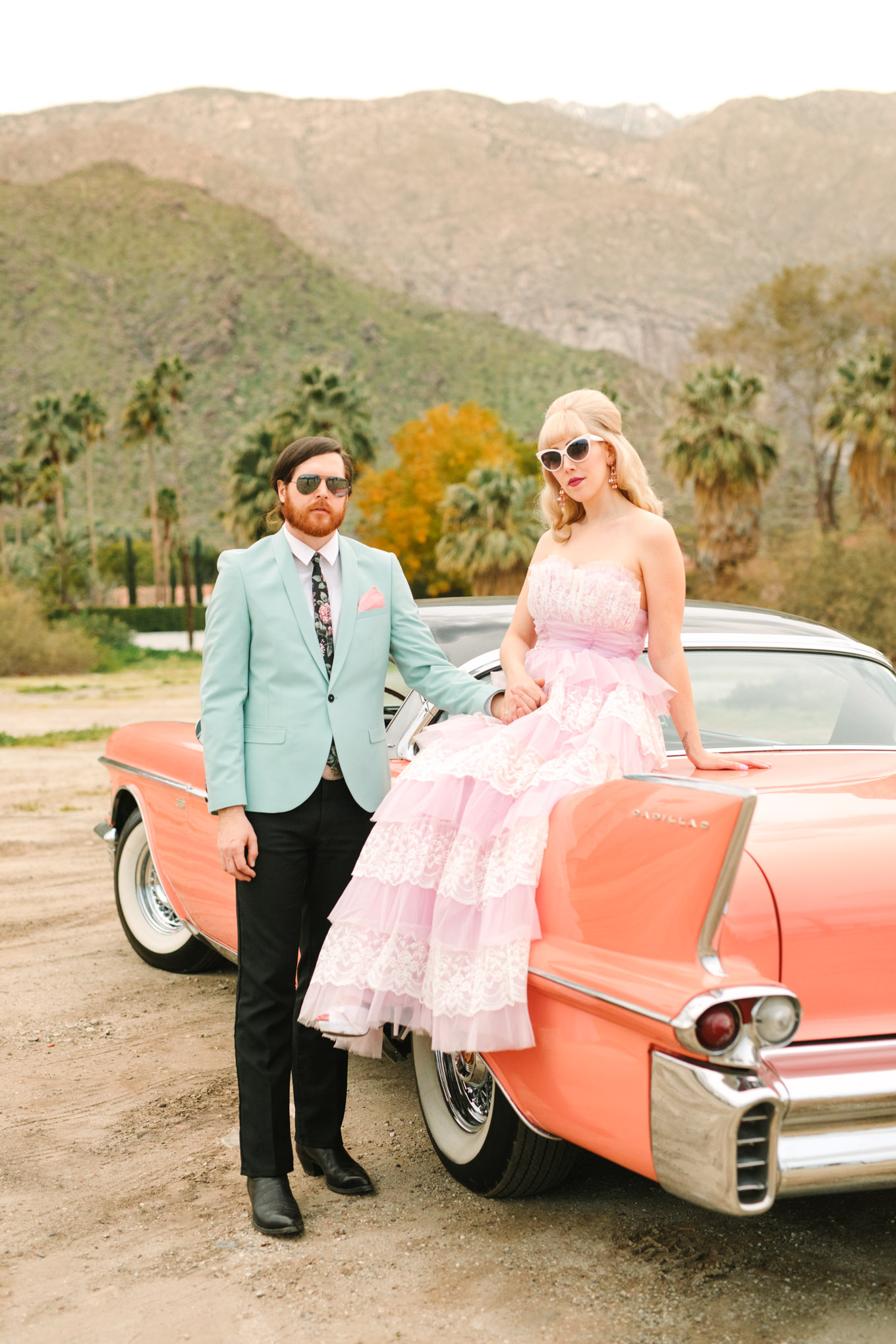 Bride and groom on the back of a retro car. Modern vintage-inspired Palm Springs engagement session with a 1960s pink Cadillac, retro clothing, and flowers by Shindig Chic. | Colorful and elevated wedding inspiration for fun-loving couples in Southern California | #engagementsession #PalmSpringsengagement #vintageweddingdress #floralcar #pinkcar   Source: Mary Costa Photography | Los Angeles