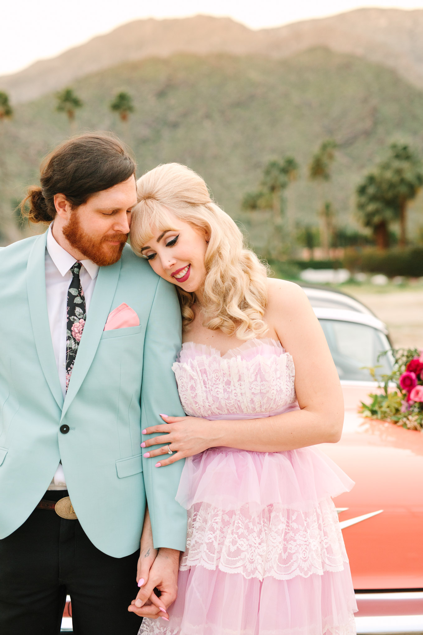 Retro couple embracing. Modern vintage-inspired Palm Springs engagement session with a 1960s pink Cadillac, retro clothing, and flowers by Shindig Chic. | Colorful and elevated wedding inspiration for fun-loving couples in Southern California | #engagementsession #PalmSpringsengagement #vintageweddingdress #floralcar #pinkcar   Source: Mary Costa Photography | Los Angeles