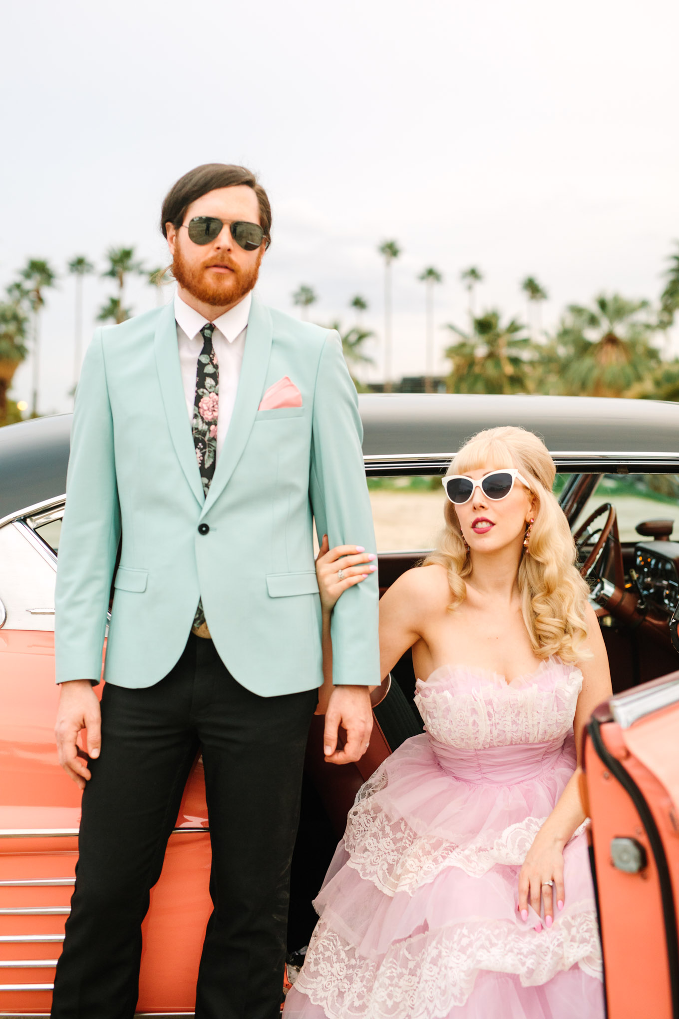 Bride and groom with classic car. Modern vintage-inspired Palm Springs engagement session with a 1960s pink Cadillac, retro clothing, and flowers by Shindig Chic. | Colorful and elevated wedding inspiration for fun-loving couples in Southern California | #engagementsession #PalmSpringsengagement #vintageweddingdress #floralcar #pinkcar   Source: Mary Costa Photography | Los Angeles
