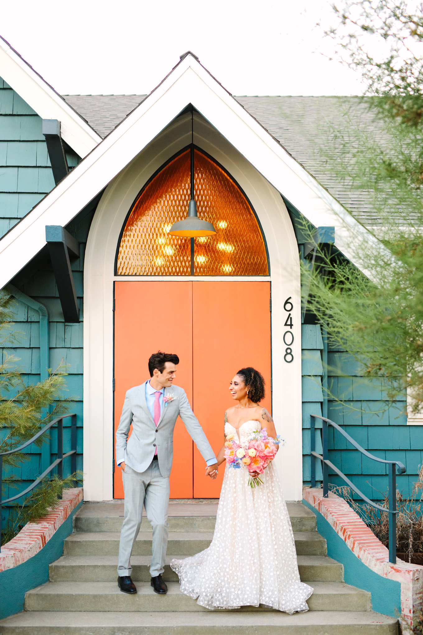 Bride and groom in front of orange doorway | Colorful pop-up micro wedding at The Ruby Street Los Angeles featured on Green Wedding Shoes | Colorful and elevated photography for fun-loving couples in Southern California | #colorfulwedding #popupwedding #weddingphotography #microwedding Source: Mary Costa Photography | Los Angeles