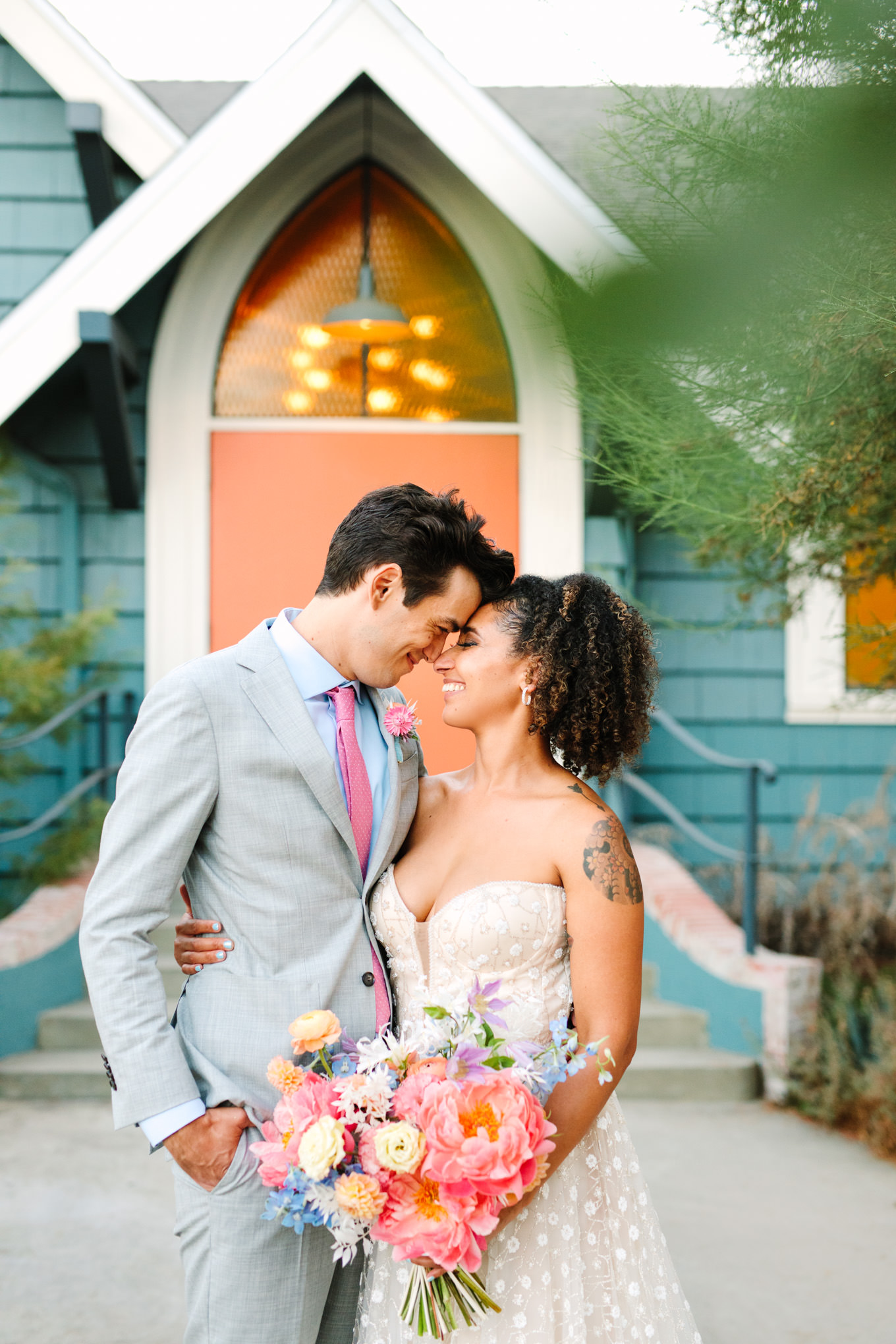 Wedding portrait of pastel couple in front of orange doorway | Colorful pop-up micro wedding at The Ruby Street Los Angeles featured on Green Wedding Shoes | Colorful and elevated photography for fun-loving couples in Southern California | #colorfulwedding #popupwedding #weddingphotography #microwedding Source: Mary Costa Photography | Los Angeles