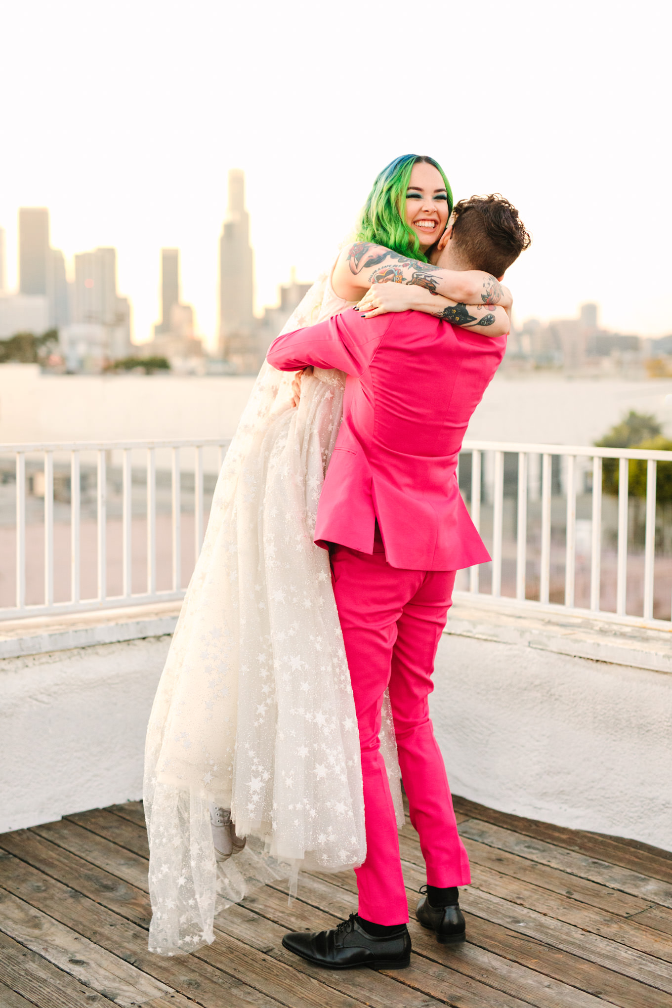 Groom in hot pink suit hugging bride with green hair on LA rooftop | Colorful wedding at The Unique Space Los Angeles published in The Knot Magazine | Fresh and colorful photography for fun-loving couples in Southern California | #colorfulwedding #losangeleswedding #weddingphotography #uniquespace Source: Mary Costa Photography | Los Angeles