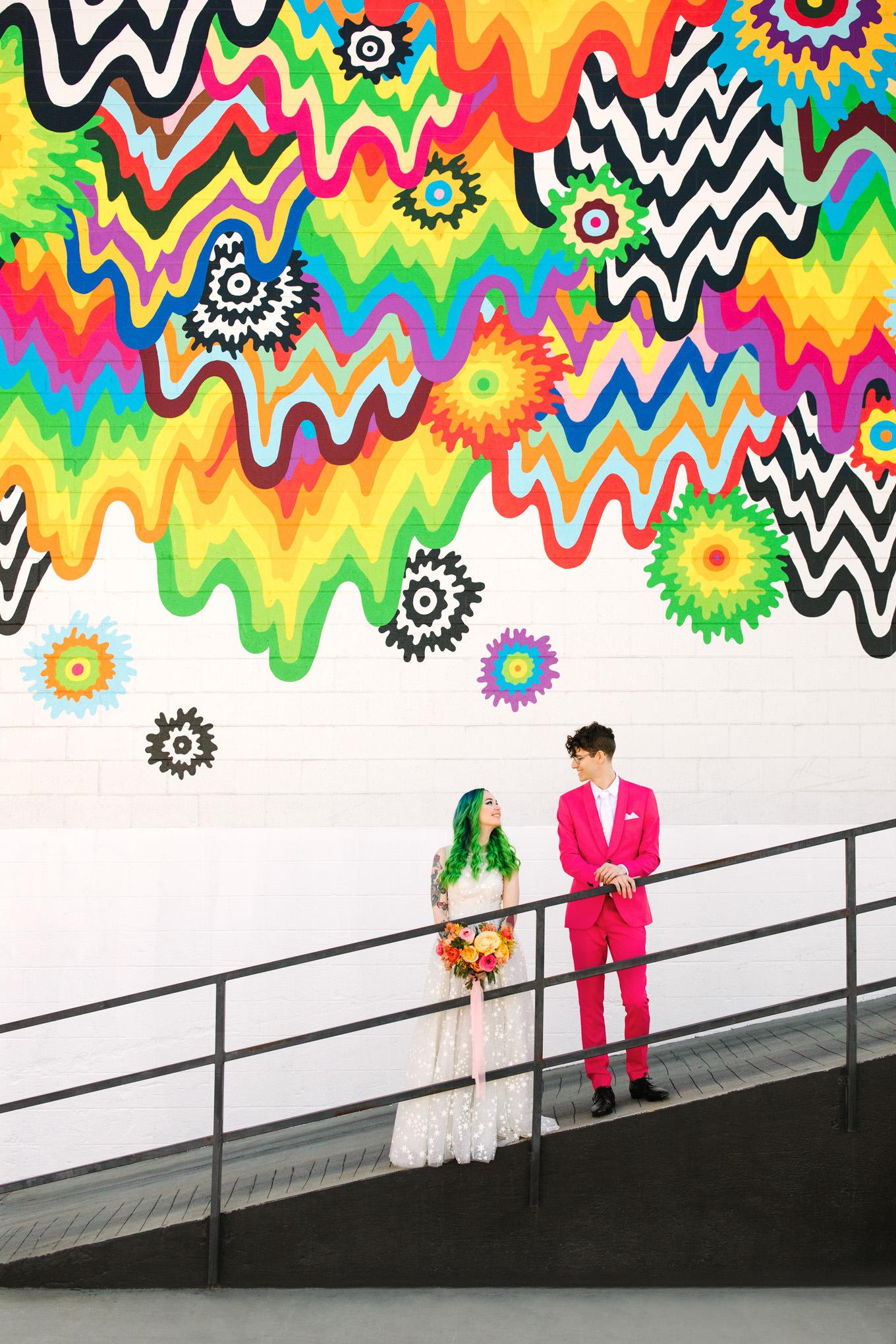 Bride with green hair and groom in pink suit in front of rainbow mural DTLA | Colorful wedding at The Unique Space Los Angeles published in The Knot Magazine | Fresh and colorful photography for fun-loving couples in Southern California | #colorfulwedding #losangeleswedding #weddingphotography #uniquespace Source: Mary Costa Photography | Los Angeles