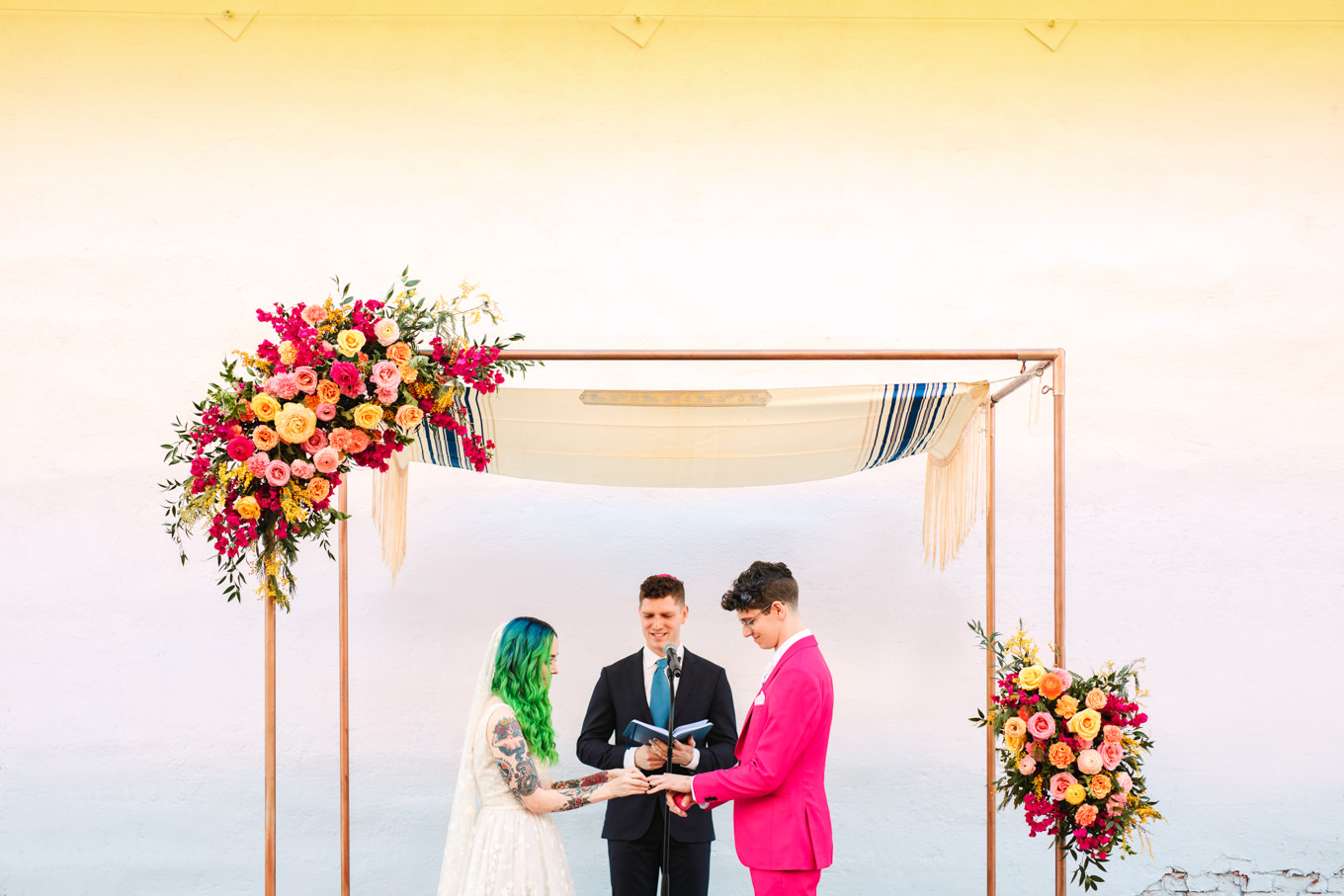 Bride with green hair putting wedding ring on groom with hot pink suit | Colorful wedding at The Unique Space Los Angeles published in The Knot Magazine | Fresh and colorful photography for fun-loving couples in Southern California | #colorfulwedding #losangeleswedding #weddingphotography #uniquespace Source: Mary Costa Photography | Los Angeles