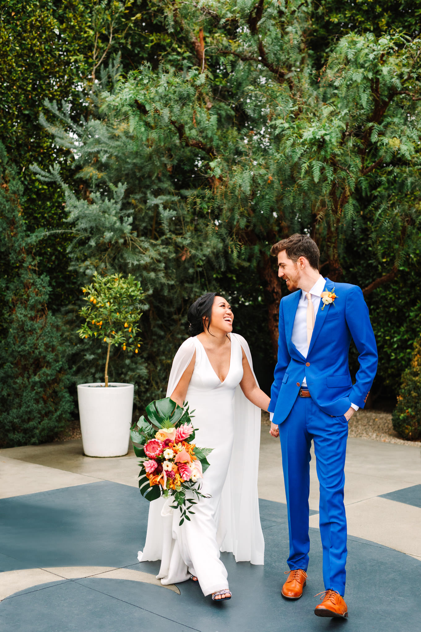 Bride in cape walking with groom in blue suit | TV inspired wedding at The Fig House Los Angeles | Published on The Knot | Fresh and colorful photography for fun-loving couples in Southern California | #losangeleswedding #TVwedding #colorfulwedding #theknot   Source: Mary Costa Photography | Los Angeles wedding photographer