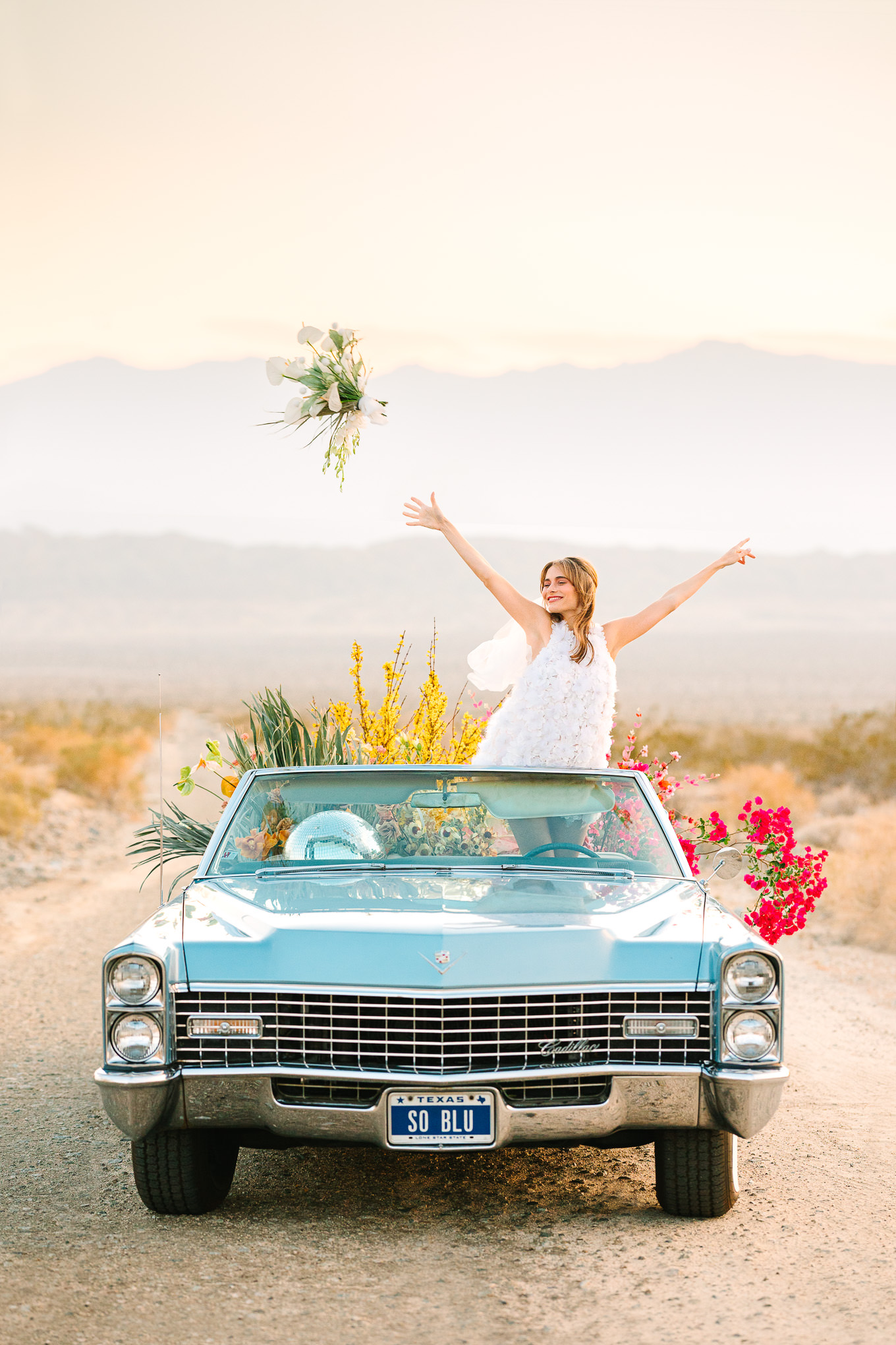 Colorful desert elopement bridal style with short Naeem Khan white dress and a blue classic car filled with flowers | Kindred Presets x Mary Costa Photography Palm Springs Ad Campaign | Colorful Palm Springs wedding photography | #palmspringsphotographer #lightroompresets #sandshotel #pinkhotel   Source: Mary Costa Photography | Los Angeles