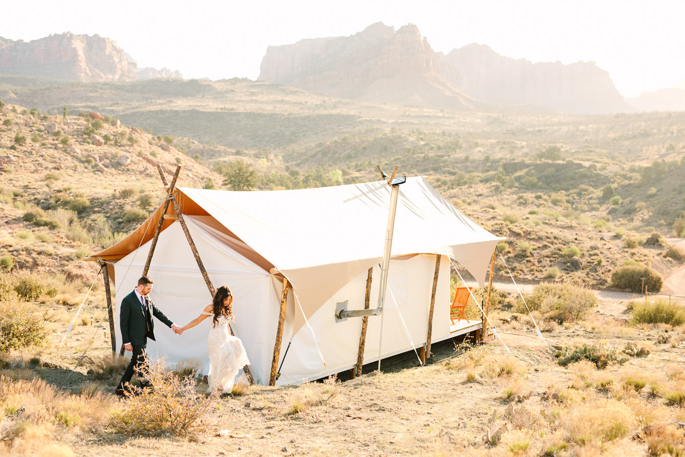 Bride and groom walking with tent | Zion Under Canvas Elopement at Sunrise | Colorful adventure elopement photography | #utahelopement #zionelopement #zionwedding #undercanvaszion #sunriseelopement  Source: Mary Costa Photography | Los Angeles