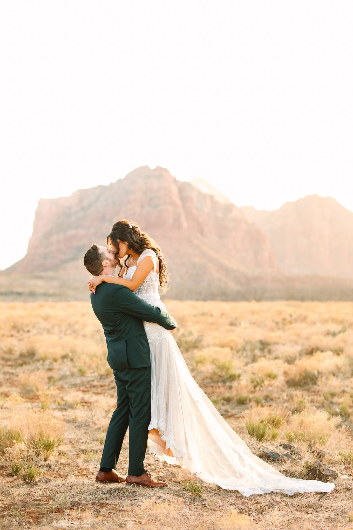 Bride kissing groom in green suit portraits | Zion Under Canvas camping elopement at sunrise | Colorful elopement photography | #utahelopement #zionelopement #zionwedding #undercanvaszion #sunriseelopement #adventureelopement  Source: Mary Costa Photography | Los Angeles