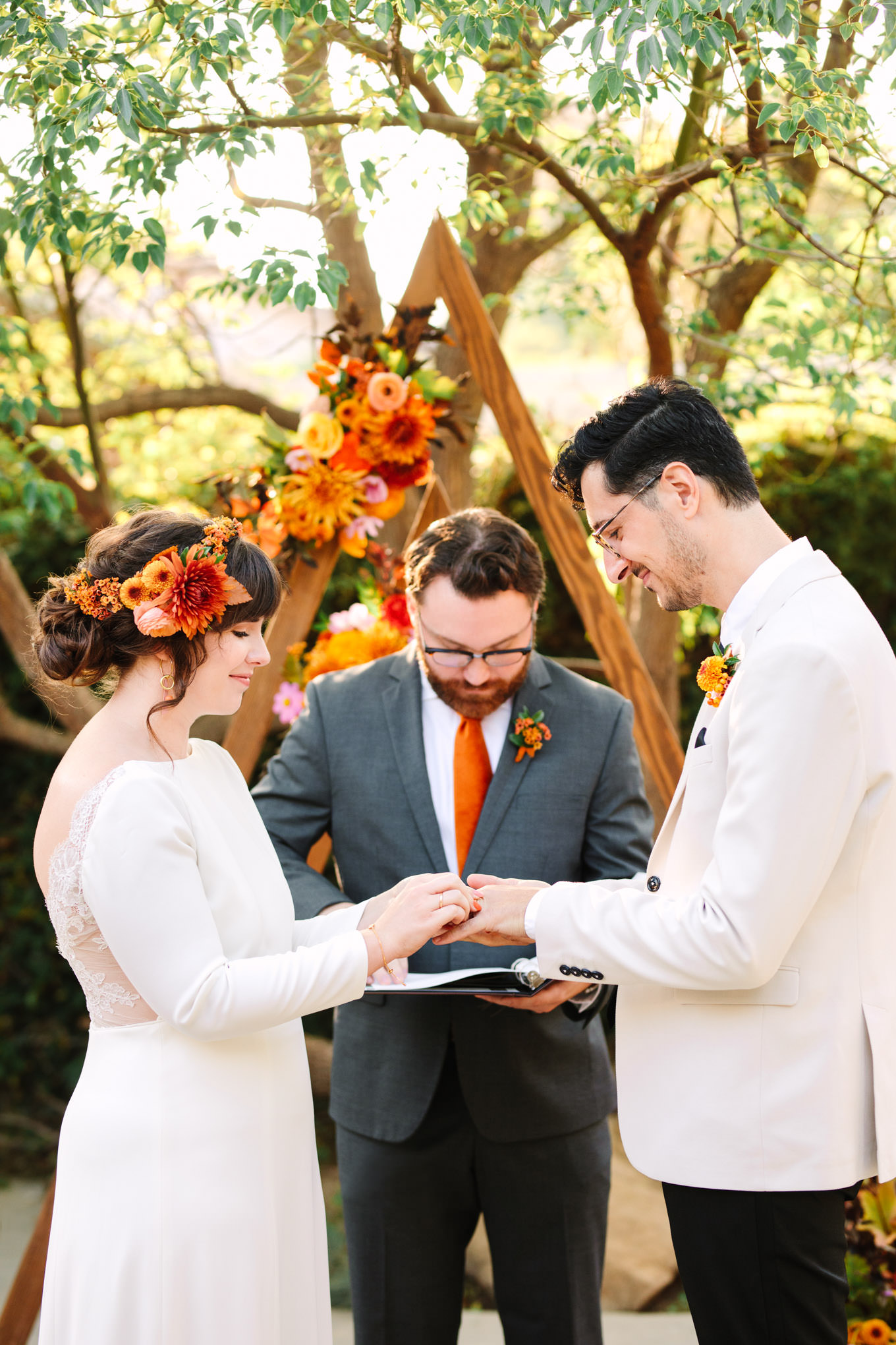 Bride putting on groom's ring with unique ceremony arch | Vibrant backyard micro wedding featured on Green Wedding Shoes | Colorful LA wedding photography | #losangeleswedding #backyardwedding #microwedding #laweddingphotographer Source: Mary Costa Photography | Los Angeles