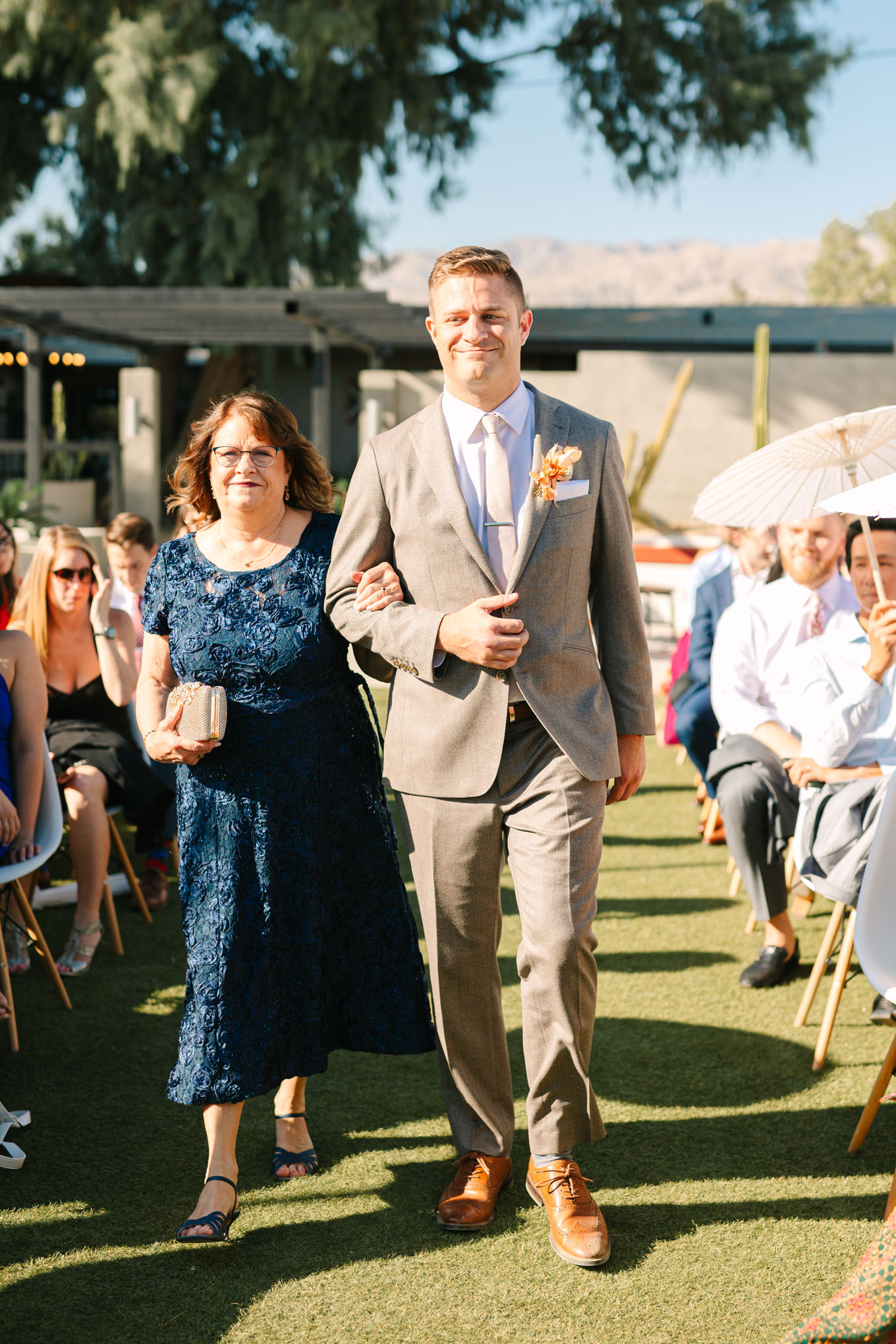 Groom walking with mom down the aisle | Pink and orange Lautner Compound wedding | Colorful Palm Springs wedding photography | #palmspringsphotographer #palmspringswedding #lautnercompound #southerncaliforniawedding  Source: Mary Costa Photography | Los Angeles
