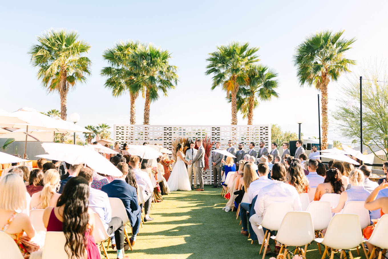 Wedding ceremony on white breeze block wall with palm trees | Pink and orange Lautner Compound wedding | Colorful Palm Springs wedding photography | #palmspringsphotographer #palmspringswedding #lautnercompound #southerncaliforniawedding  Source: Mary Costa Photography | Los Angeles