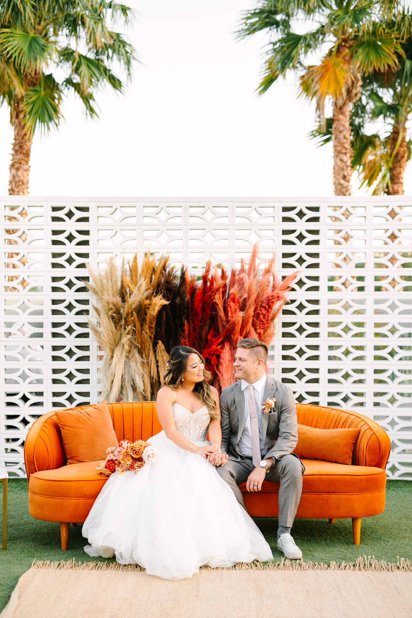 Bride and groom on orange velvet couch | Pink and orange Lautner Compound wedding | Colorful Palm Springs wedding photography | #palmspringsphotographer #palmspringswedding #lautnercompound #southerncaliforniawedding  Source: Mary Costa Photography | Los Angeles