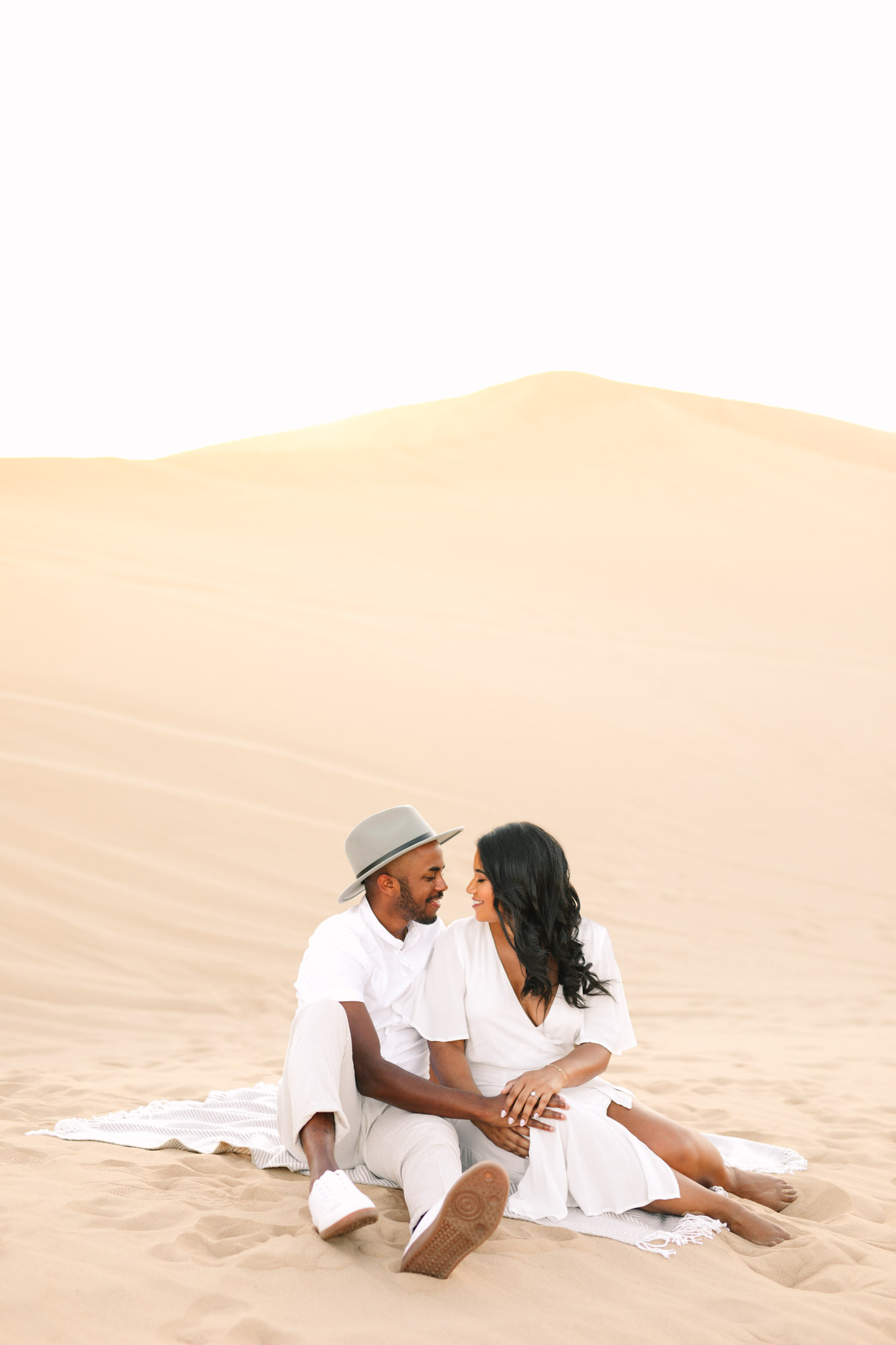 Engaged couple sitting on a blanket in the sand dunes | California Sand Dunes engagement session | Colorful Palm Springs wedding photography | #palmspringsphotographer #sanddunes #engagementsession #southerncalifornia  Source: Mary Costa Photography | Los Angeles