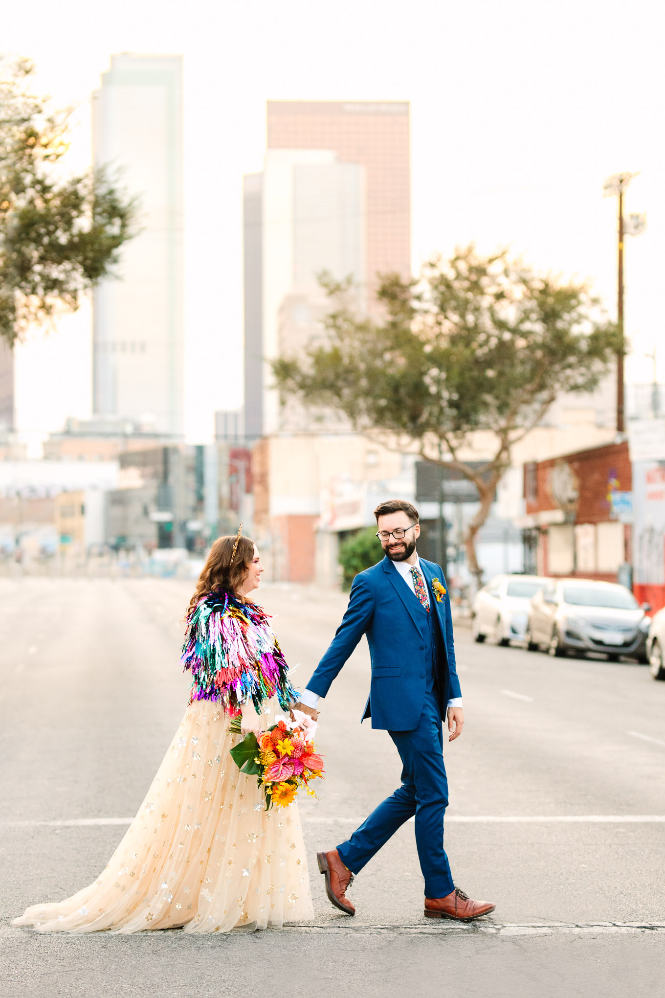 Bride and groom walking with LA skyline behind them | Colorful Downtown Los Angeles Valentine Wedding | Los Angeles wedding photographer | #losangeleswedding #colorfulwedding #DTLA #valentinedtla   Source: Mary Costa Photography | Los Angeles