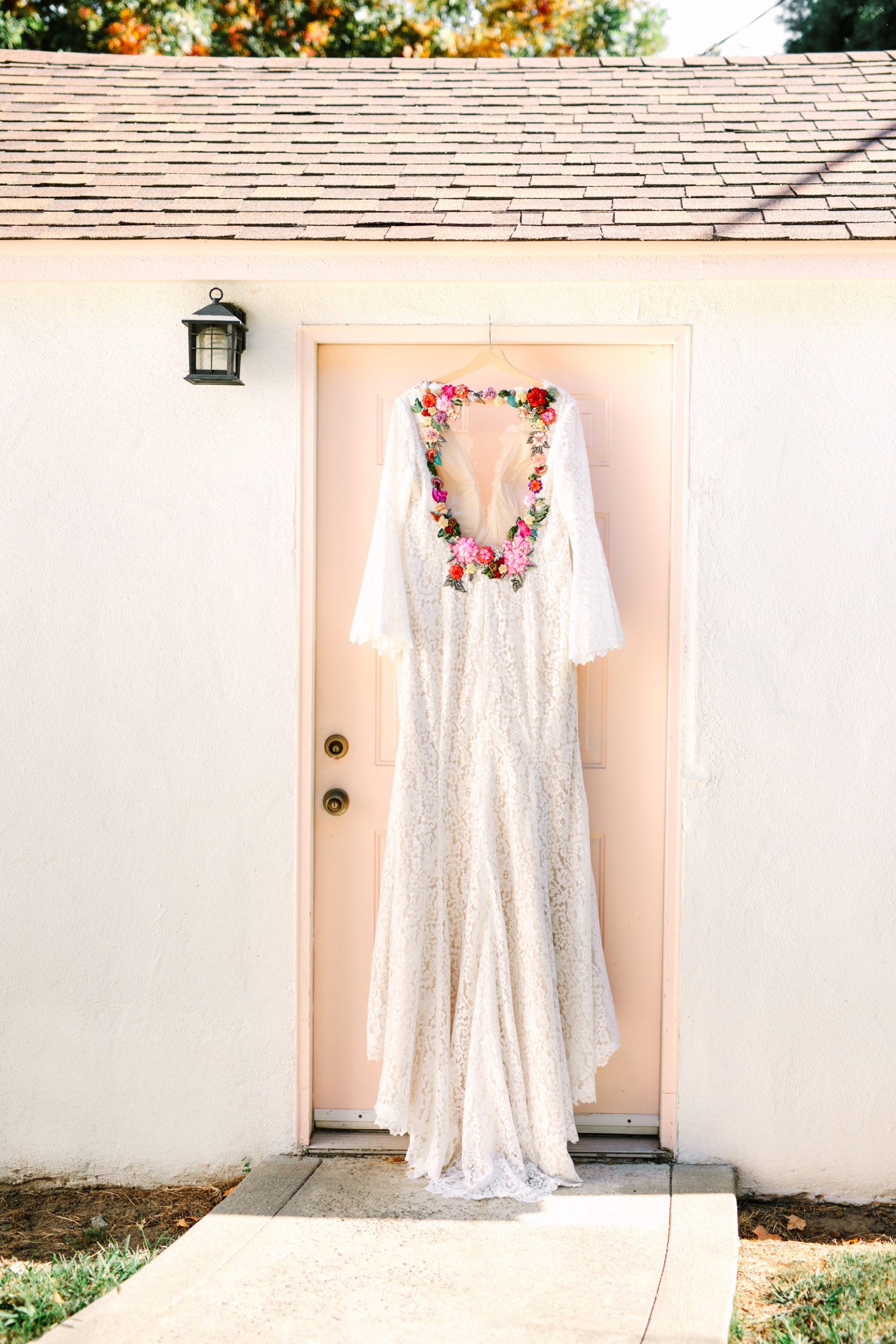 Custom bridal gown with colorful embroidered flowers by Heirloom Bride hanging on pink door - www.marycostaweddings.com