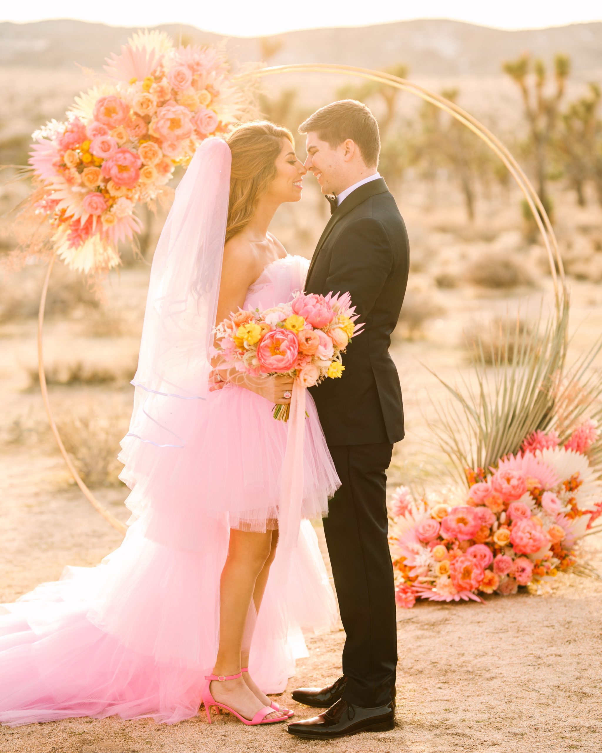Bride and groom in front of circular ceremony arch | Pink wedding dress Joshua Tree elopement featured on Green Wedding Shoes | Colorful desert wedding inspiration for fun-loving couples in Southern California #joshuatreewedding #joshuatreeelopement #pinkwedding #greenweddingshoes Source: Mary Costa Photography | Los Angeles
