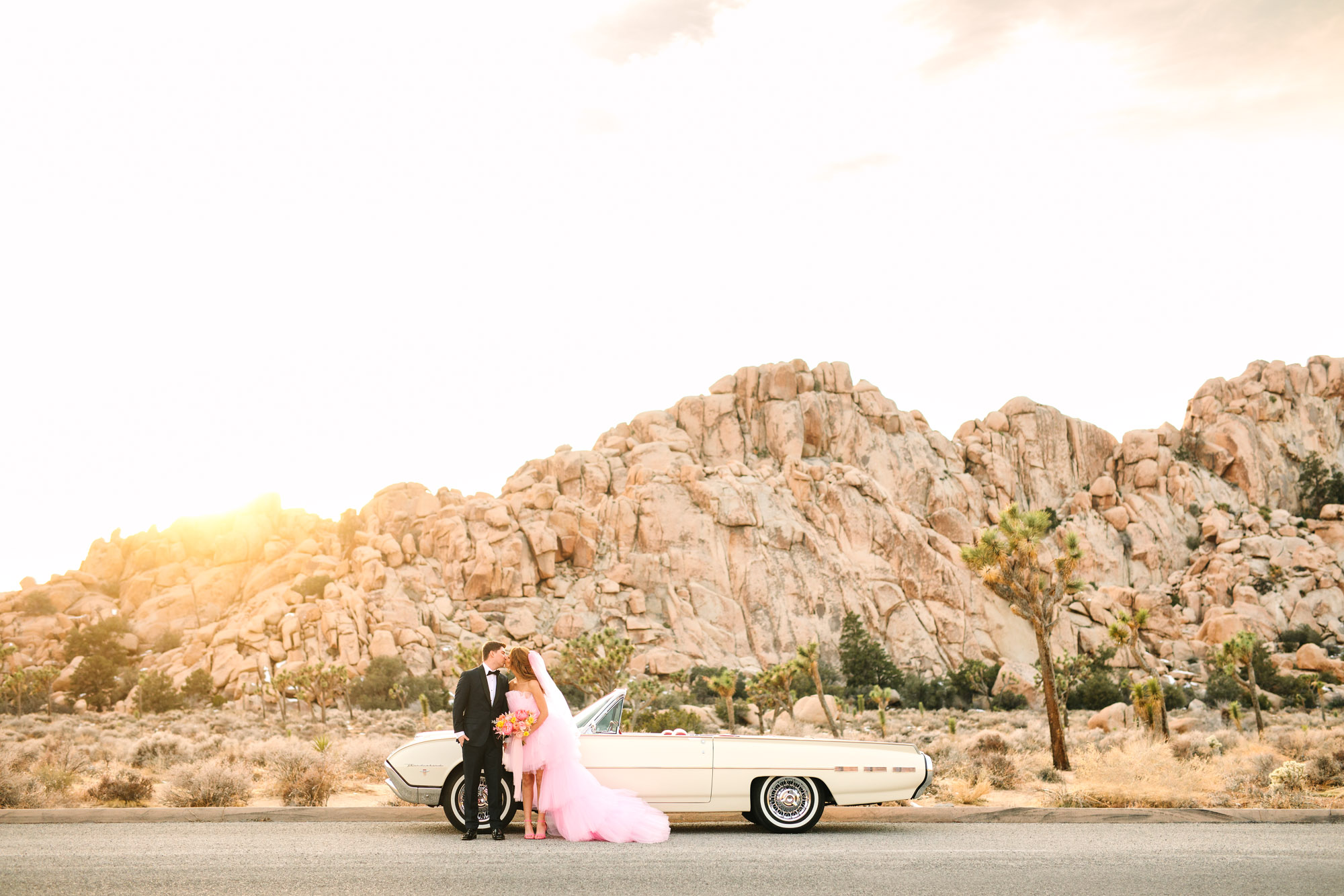 Bride and groom with white classic Ford Thunderbird convertible | Pink wedding dress Joshua Tree elopement featured on Green Wedding Shoes | Colorful desert wedding inspiration for fun-loving couples in Southern California #joshuatreewedding #joshuatreeelopement #pinkwedding #greenweddingshoes Source: Mary Costa Photography | Los Angeles