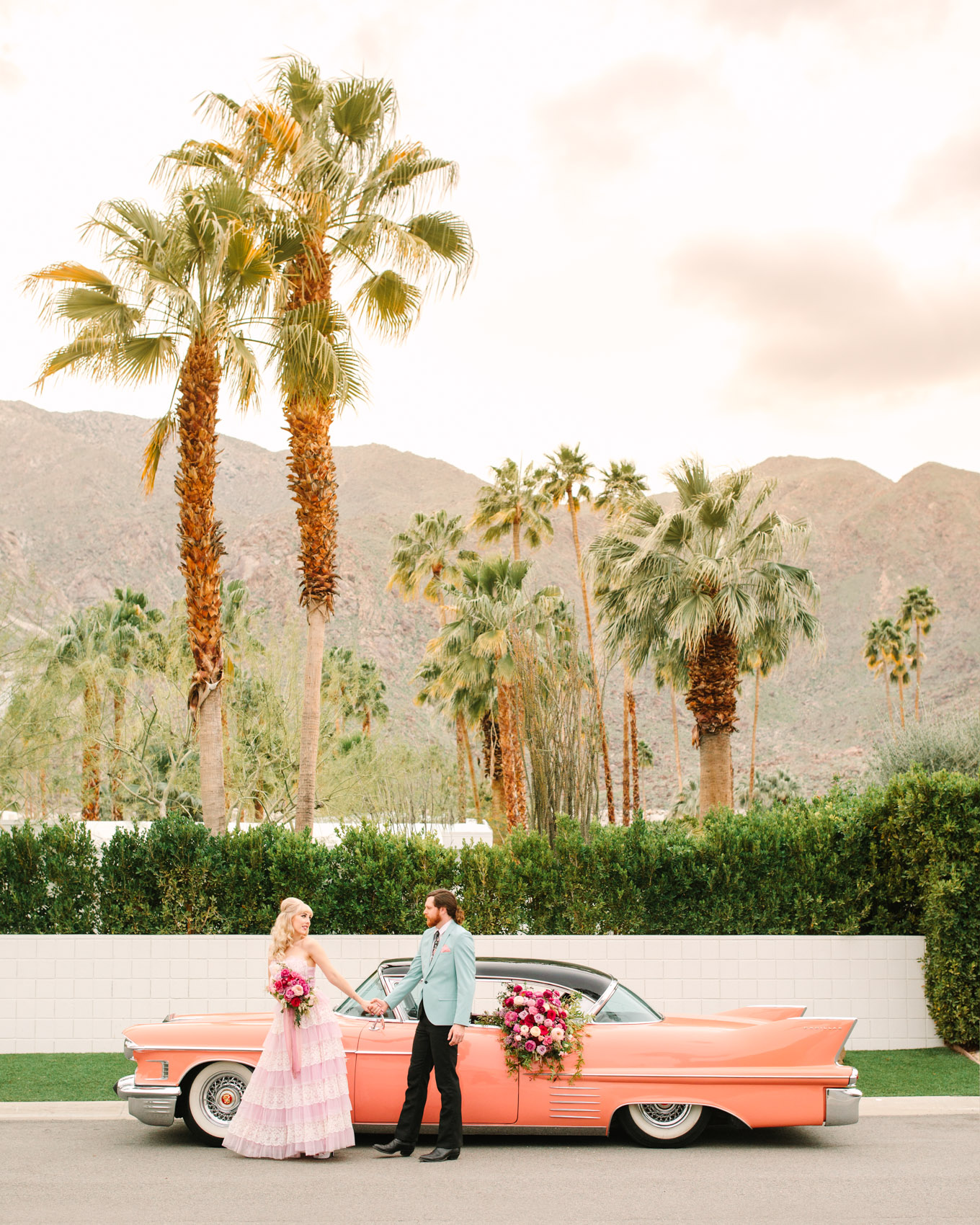 Modern vintage-inspired Palm Springs engagement session with a 1960s pink Cadillac car, retro clothing, and flowers by Shindig Chic. | Colorful and elevated wedding inspiration for fun-loving couples in Southern California | #engagementsession #PalmSpringsengagement #vintageweddingdress #floralcar #pinkcar   Source: Mary Costa Photography | Los Angeles
