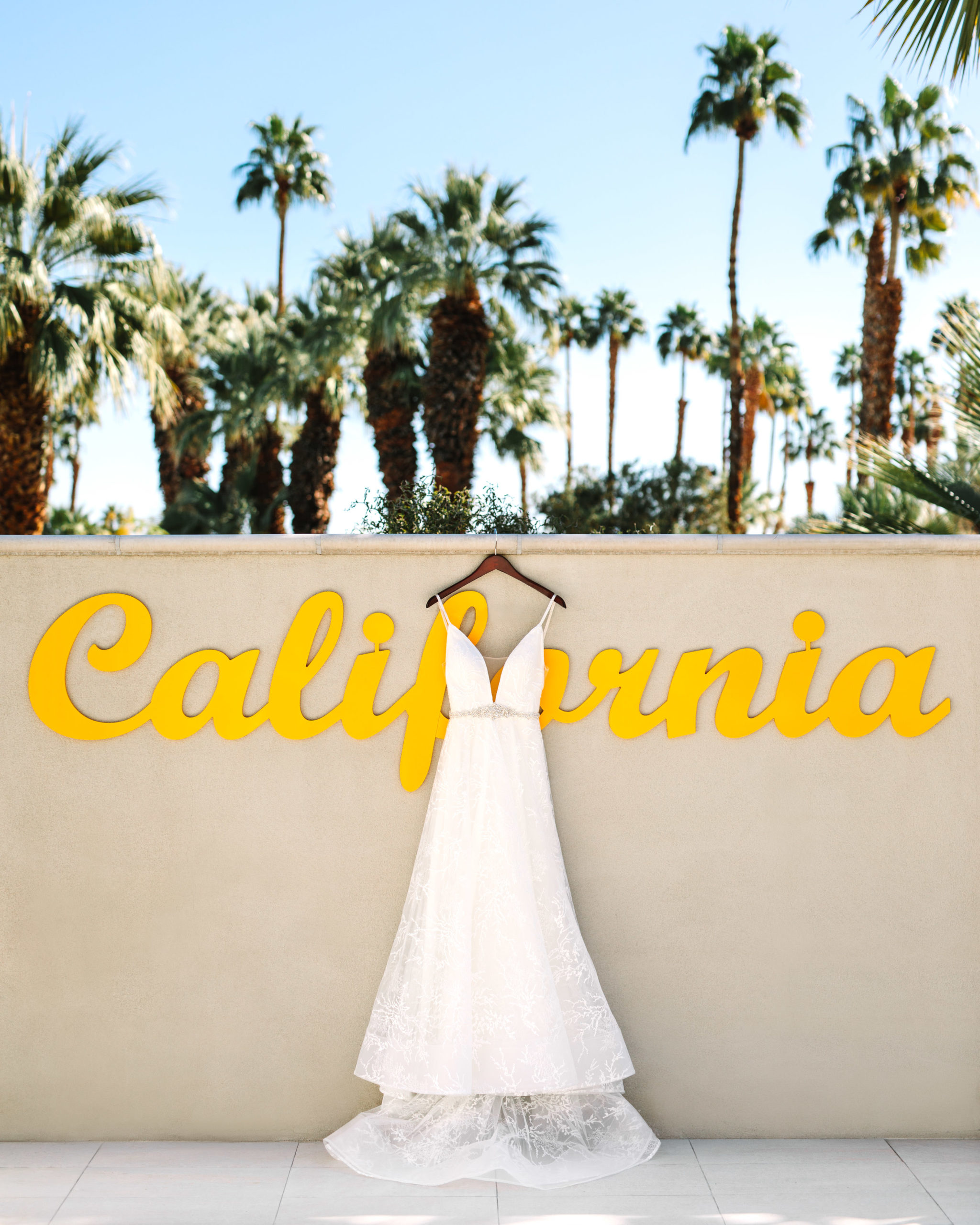 Dress hanging on yellow California sign at Hotel Paseo | Living Desert Zoo & Gardens wedding with unique details | Elevated and colorful wedding photography for fun-loving couples in Southern California | #PalmSprings #palmspringsphotographer #gardenwedding #palmspringswedding Source: Mary Costa Photography | Los Angeles wedding photographer