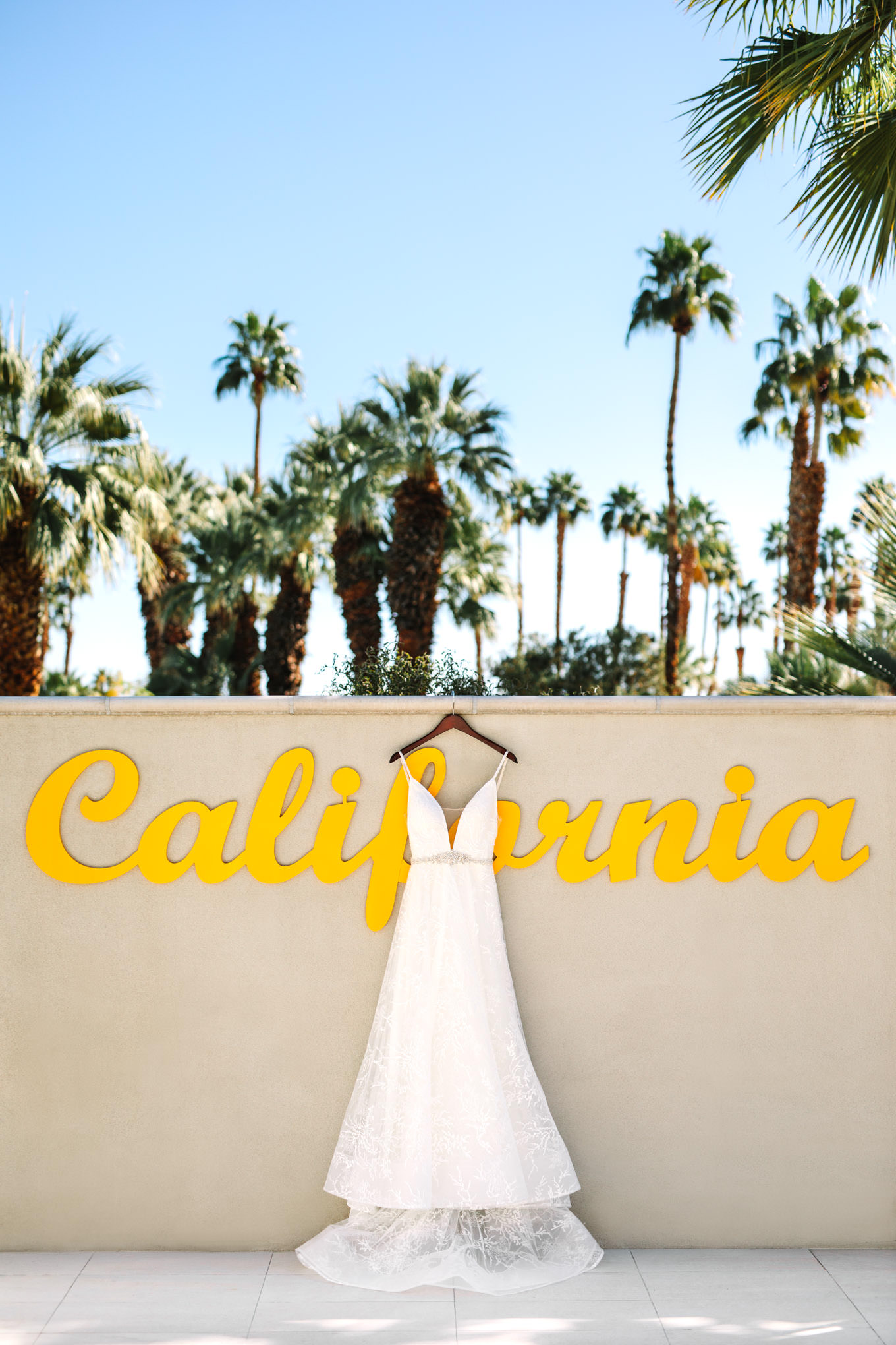 Wedding dress hanging on California sign at Hotel Paseo | Living Desert Zoo & Gardens wedding with unique details | Elevated and colorful wedding photography for fun-loving couples in Southern California |  #PalmSprings #palmspringsphotographer #gardenwedding #palmspringswedding  Source: Mary Costa Photography | Los Angeles wedding photographer 